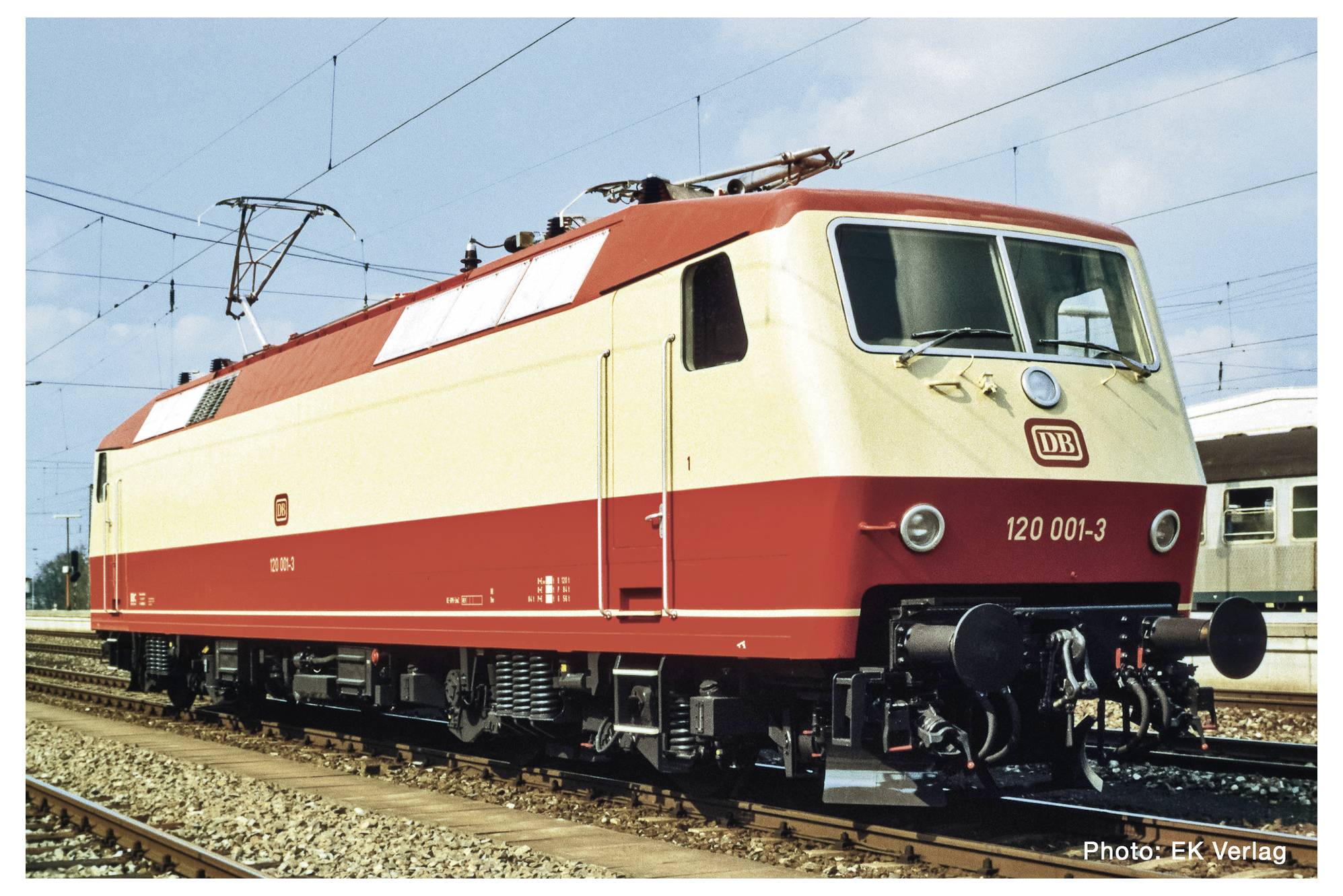 Un train électrique rouge et beige de la Deutsche Bahn est stationné sur des voies par une journée ensoleillée. D'autres voies ferrées sont visibles en arrière-plan.