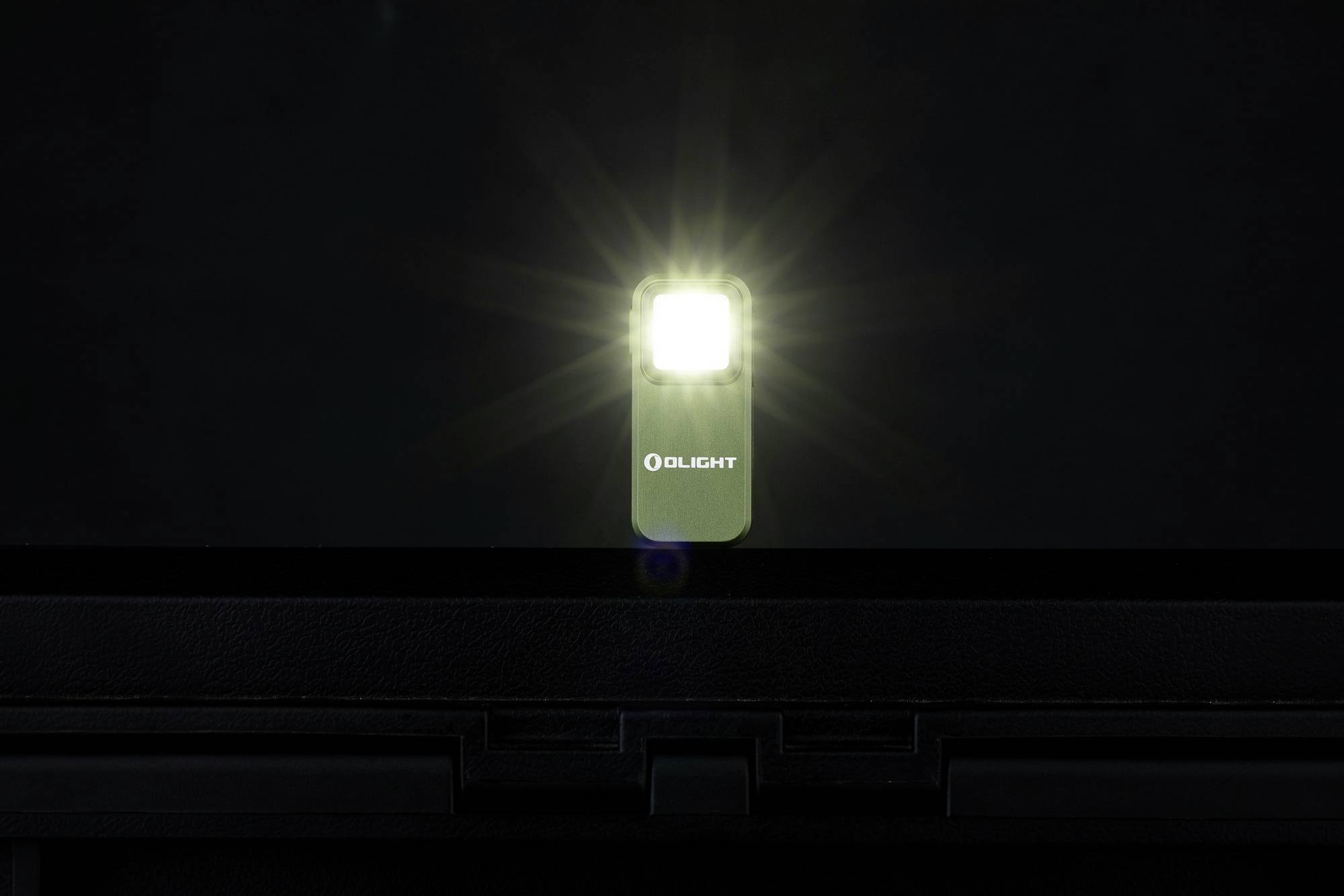 Une lampe de poche Olight lumineuse devant un arrière-plan sombre, la lumière rayonnant de la lampe, la marque 'Olight' visible sur le devant.
