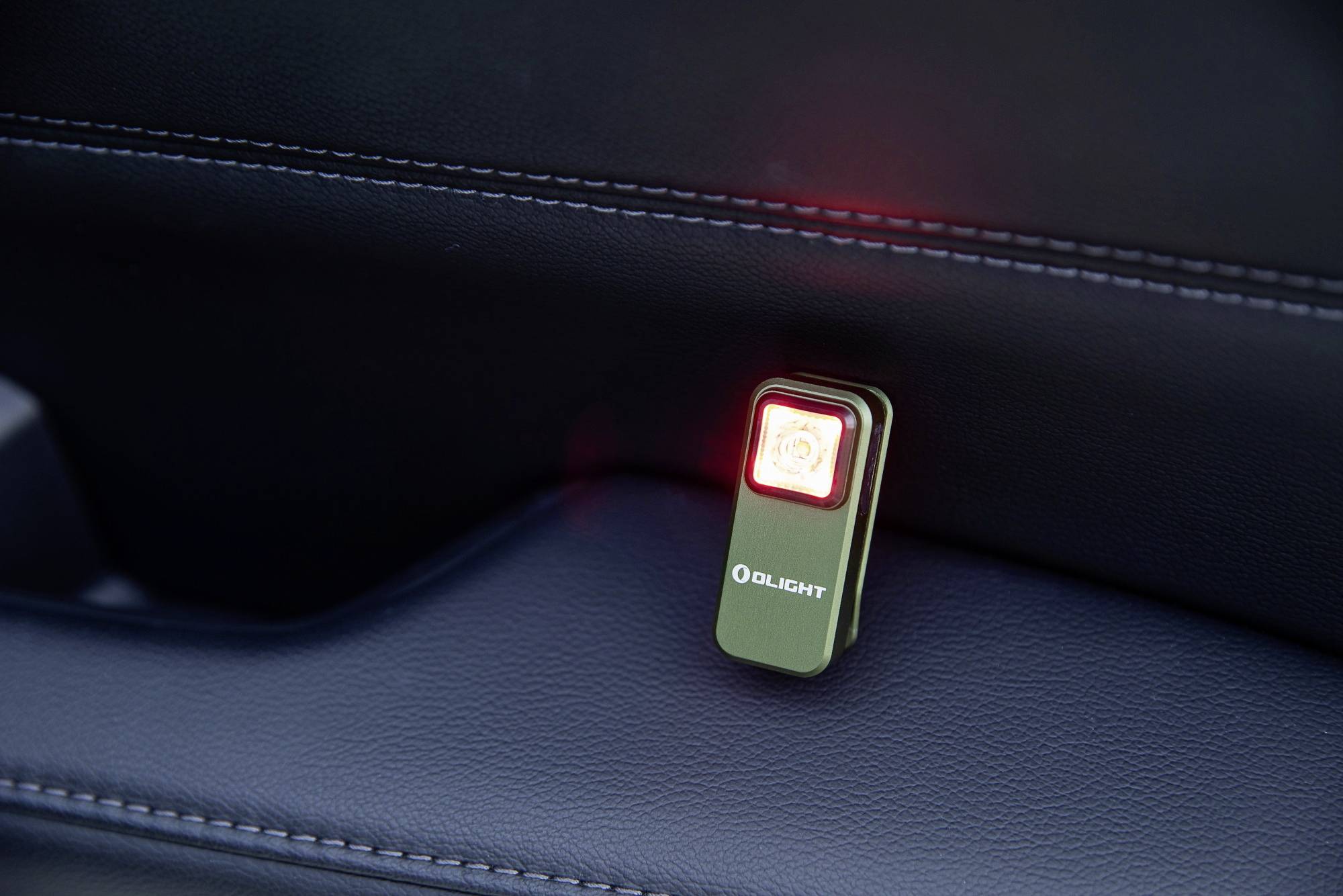 Un petit appareil rectangulaire Olight avec une lumière rouge brille sur une surface sombre à l'intérieur d'un véhicule.