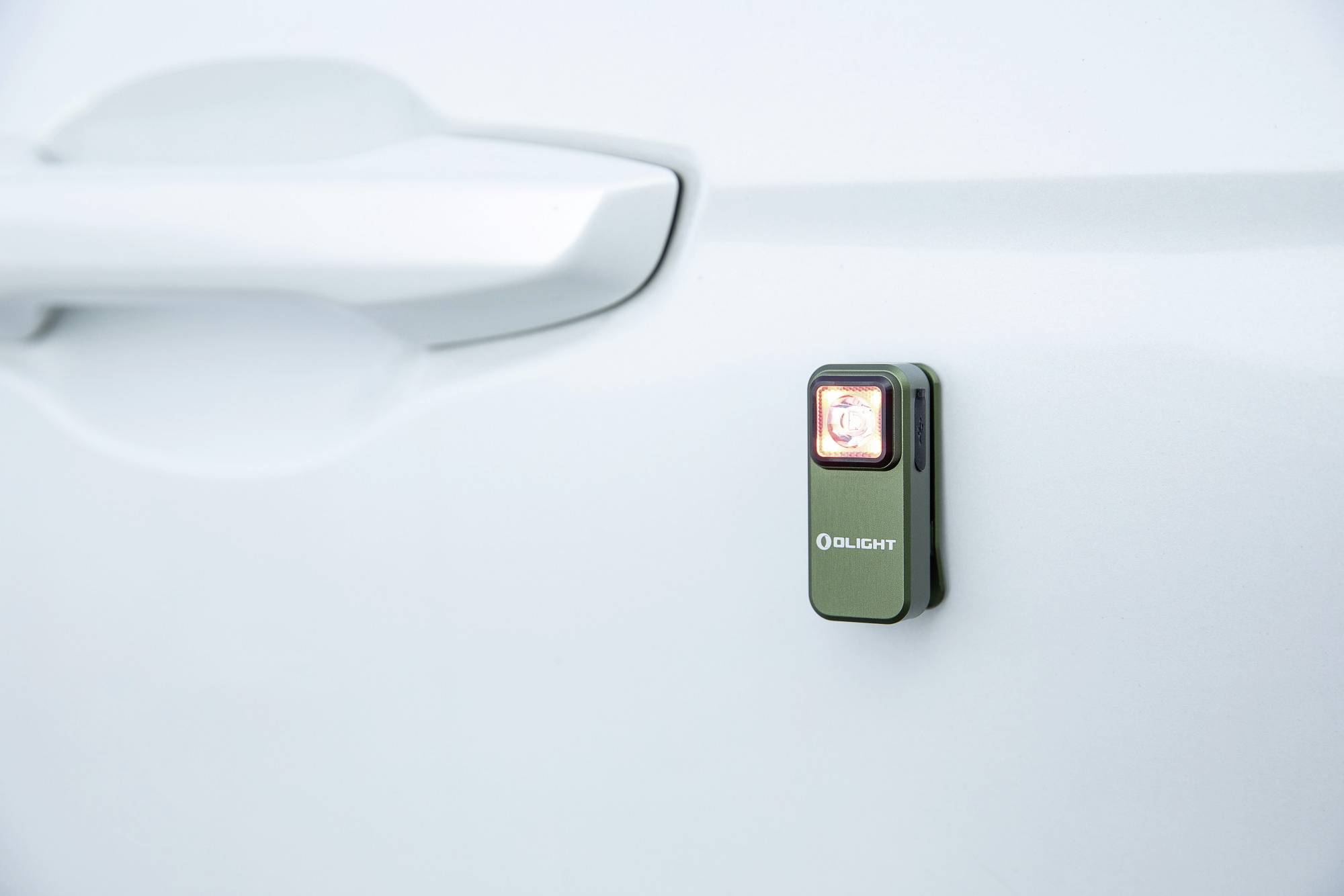 Une petite lampe verte de 'Olight' est fixée à une portière de voiture et brille en rouge.