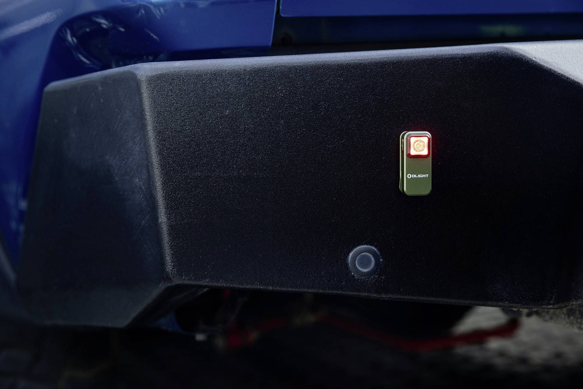 Un grand appareil noir avec un petit voyant rouge lumineux au centre, fixé à l'arrière d'un véhicule bleu.