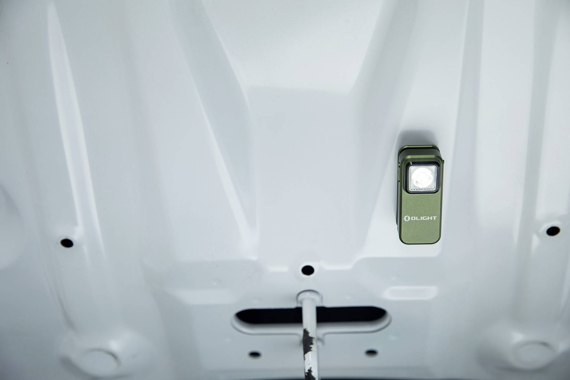 Une lampe de poche verte brille sous le capot d'une voiture et éclaire le compartiment moteur.