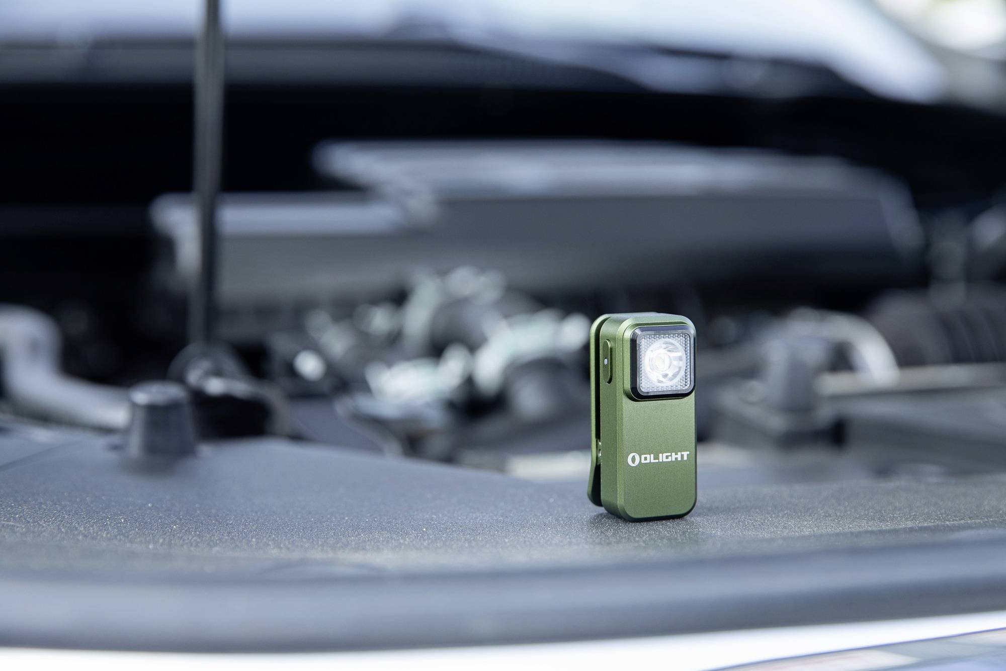 Une petite lampe de poche verte est posée sur le moteur d'une voiture. À l'arrière-plan, on aperçoit un compartiment moteur flou.