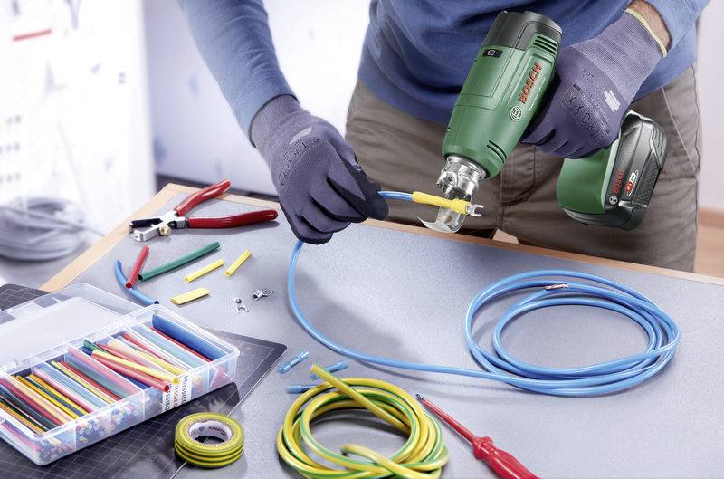 Un électricien travaille sur un câble avec une perceuse, une pince et des connecteurs de câble sur une table, entouré d'outils.