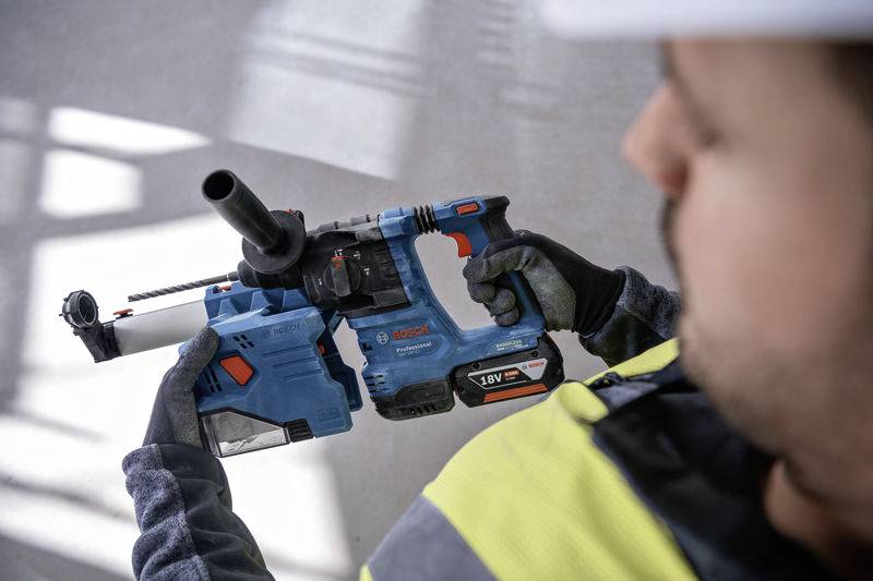 Une personne tient un marteau-perforateur bleu avec une poignée noire. La personne porte des équipements de sécurité, y compris des gants et un casque.