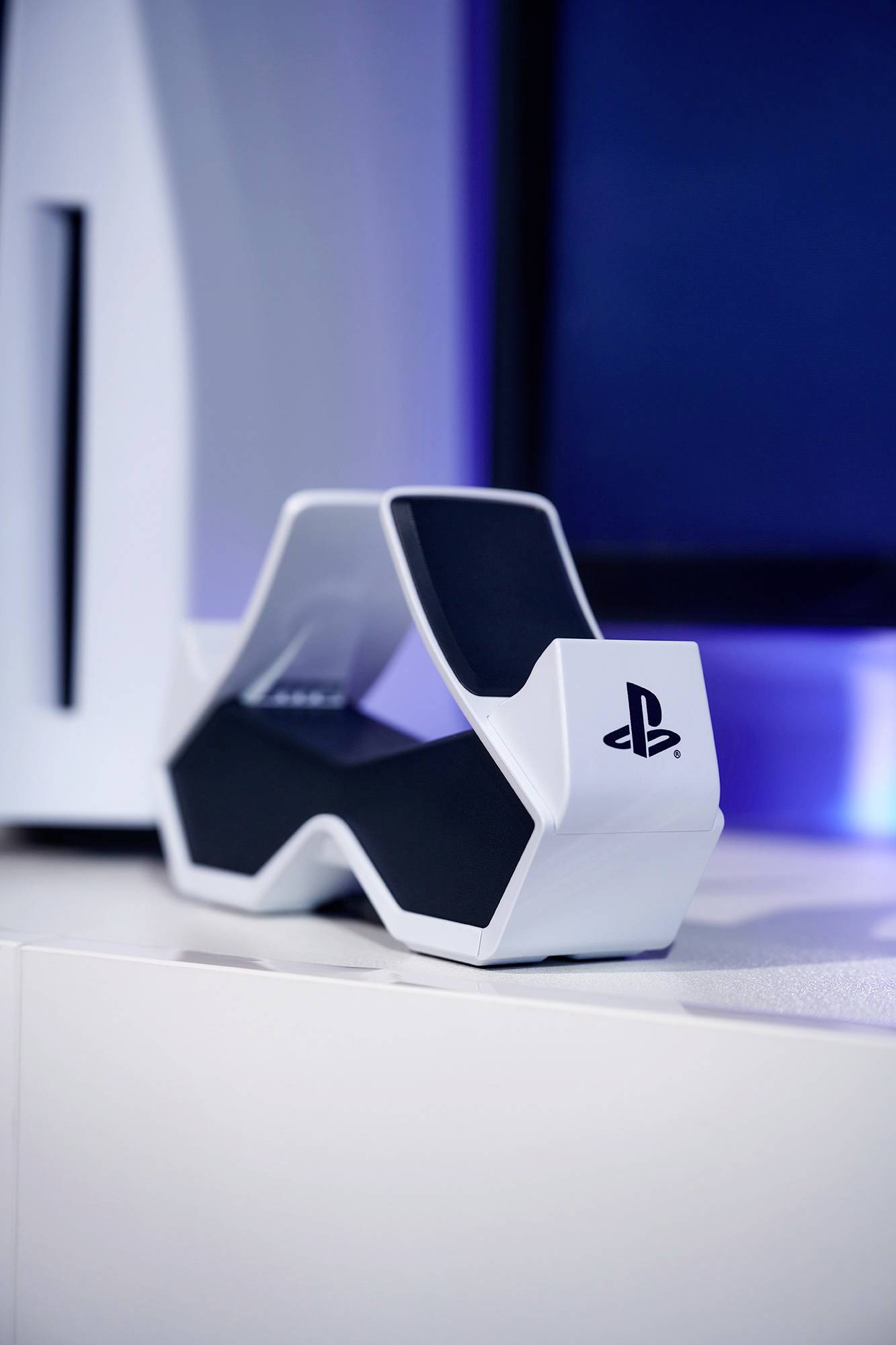 Une station de contrôleur PlayStation blanche devant un fond bleu, avec une partie d'une console visible à gauche de l'image.
