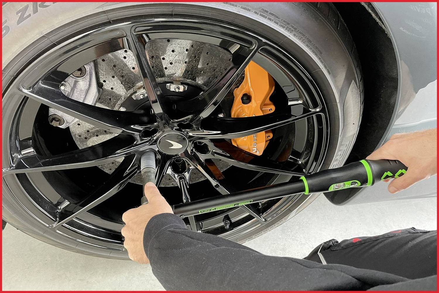 Une personne serre les écrous de roue avec une clé dynamométrique sur une voiture noire dont l'étrier de frein est orange.