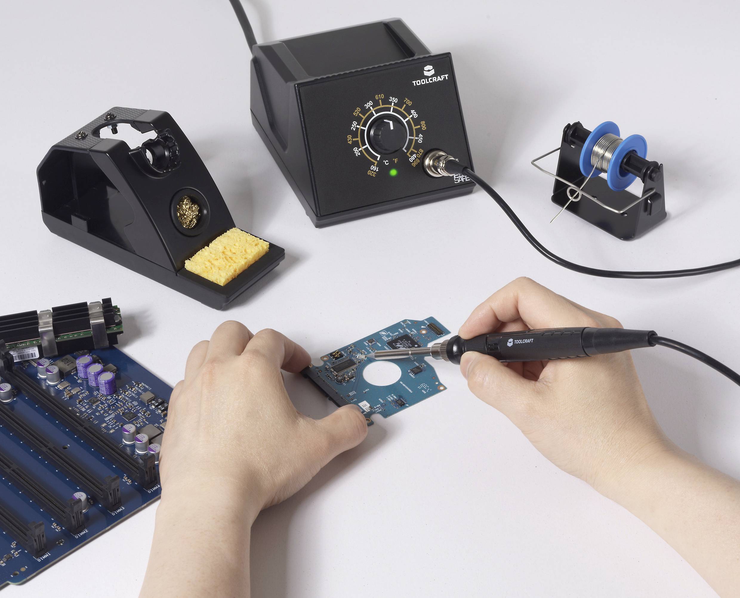 Une personne soudant des composants électroniques sur une carte de circuit imprimé à l'aide d'un fer à souder, avec une station de soudage et un rouleau à proximité.