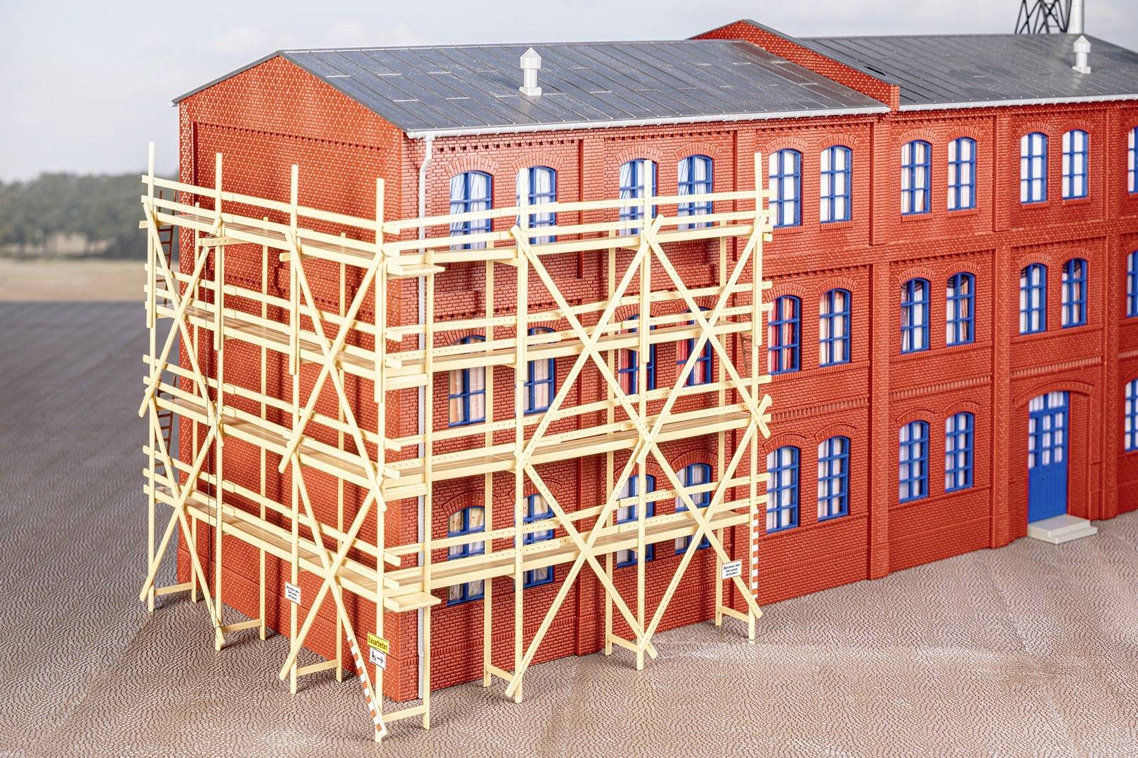 Bâtiment en brique avec des fenêtres peintes en bleu. Au premier plan, un échafaudage en bois est installé, s'étendant sur plusieurs étages.