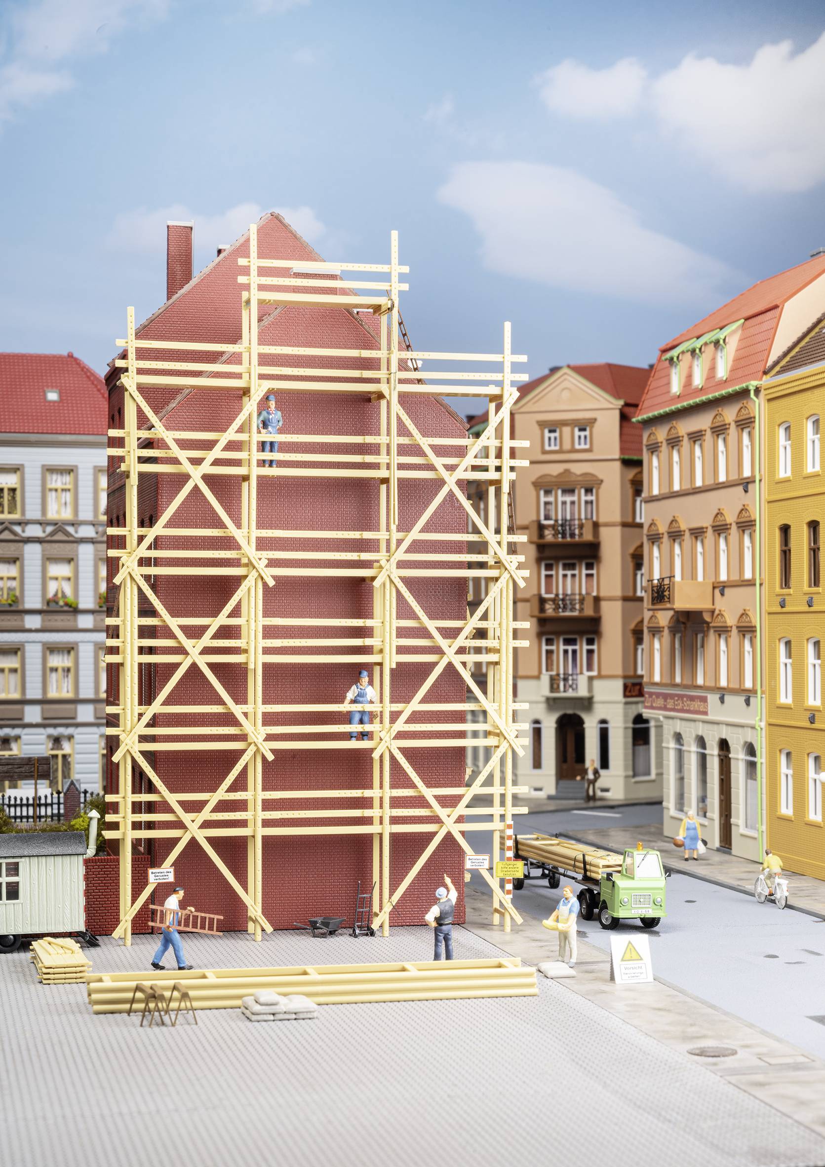 Une maquette d'un chantier de construction dans une ville avec un bâtiment en échafaudages, des ouvriers et un petit camion au premier plan.