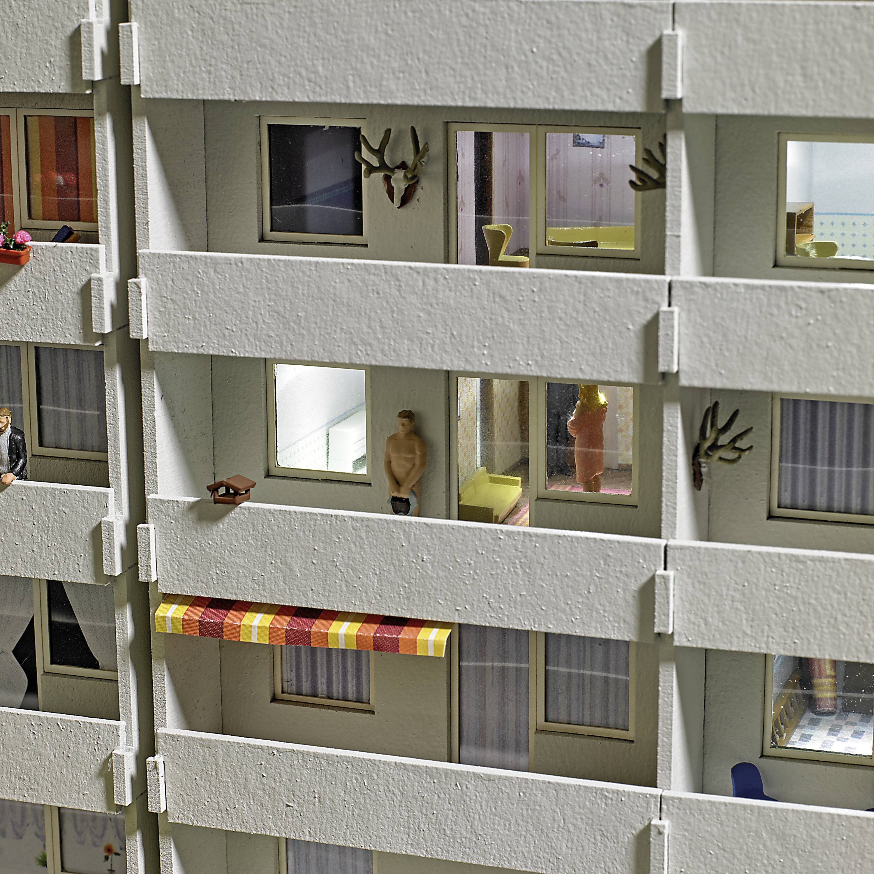 Un immeuble d'habitation la nuit avec des appartements éclairés. Certaines fenêtres montrent des personnes et des décorations. Les balcons ont des designs différents.