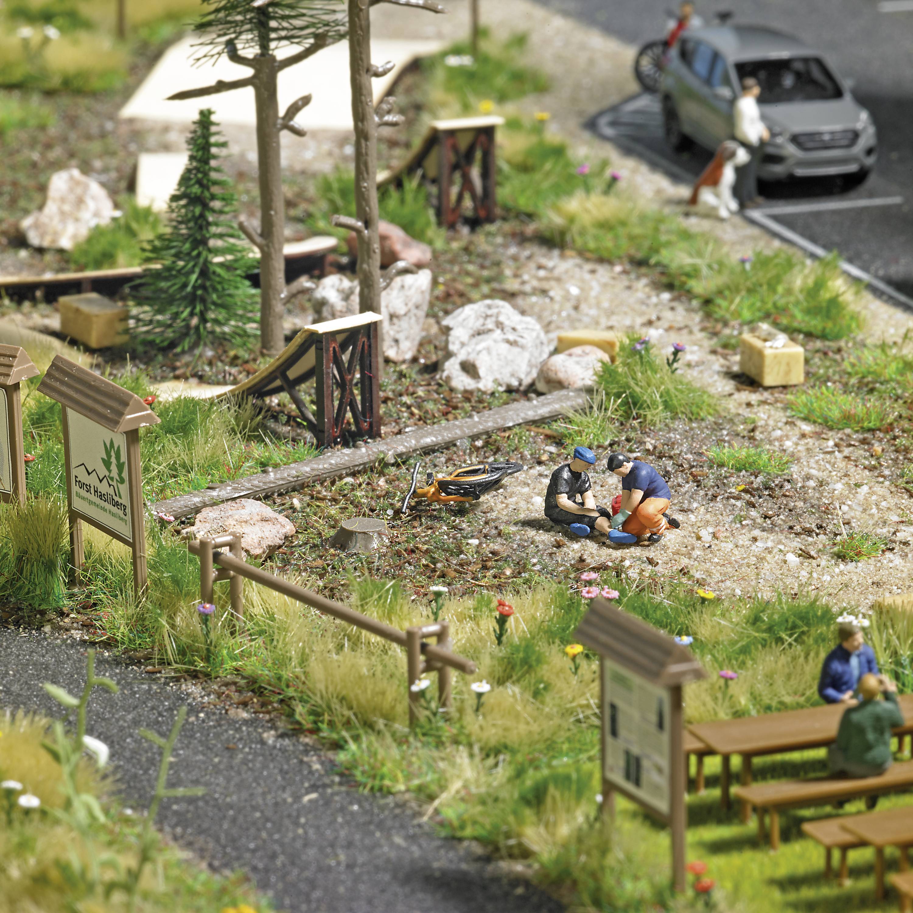 Un mini-diorama représente une scène de parc avec des personnes, des arbres et un étang. Deux personnages au centre sont absorbés dans une conversation.