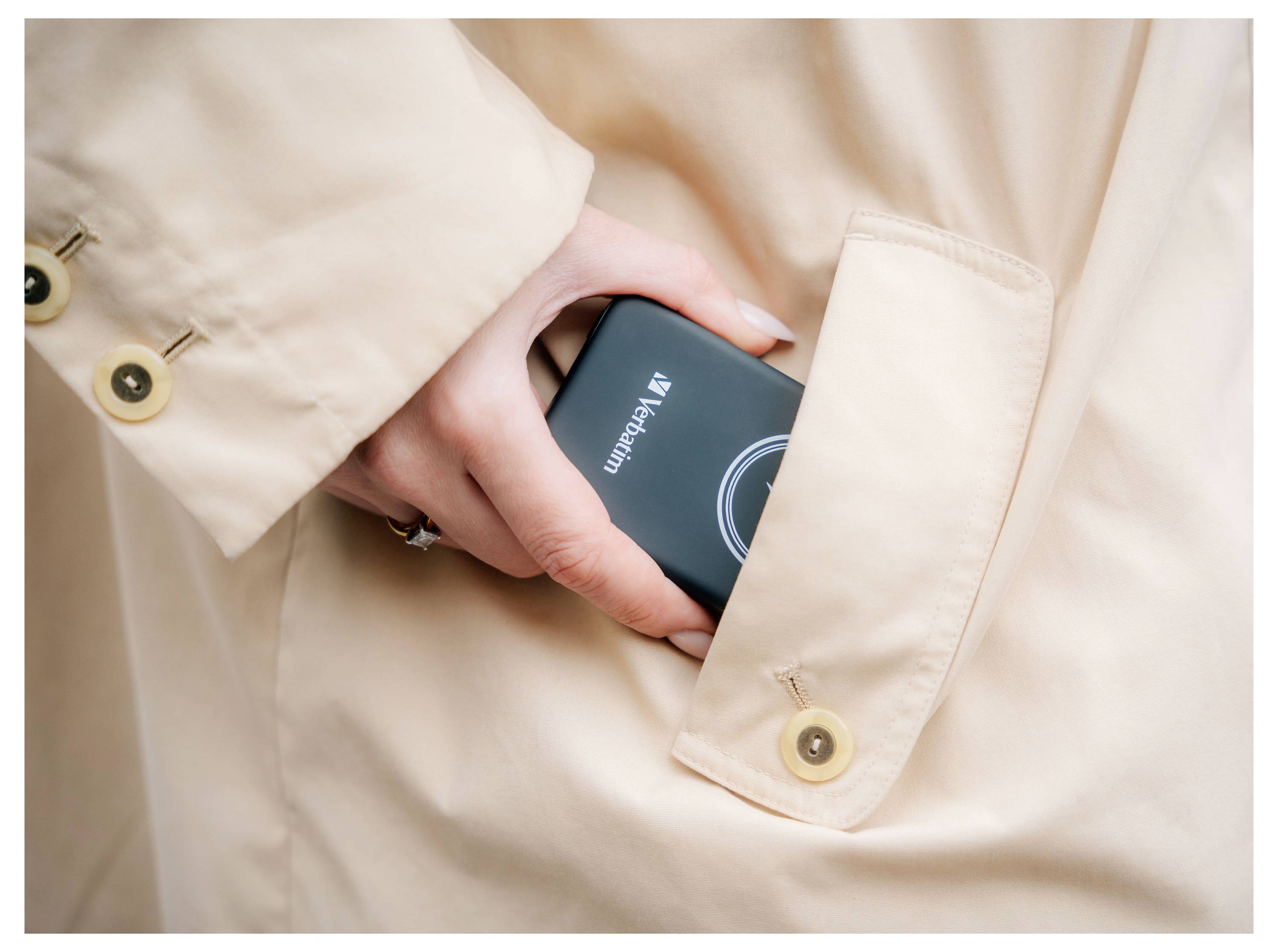 Une main gantée d'un manteau beige glisse un disque dur portable noir de la marque Verbatim dans une poche.