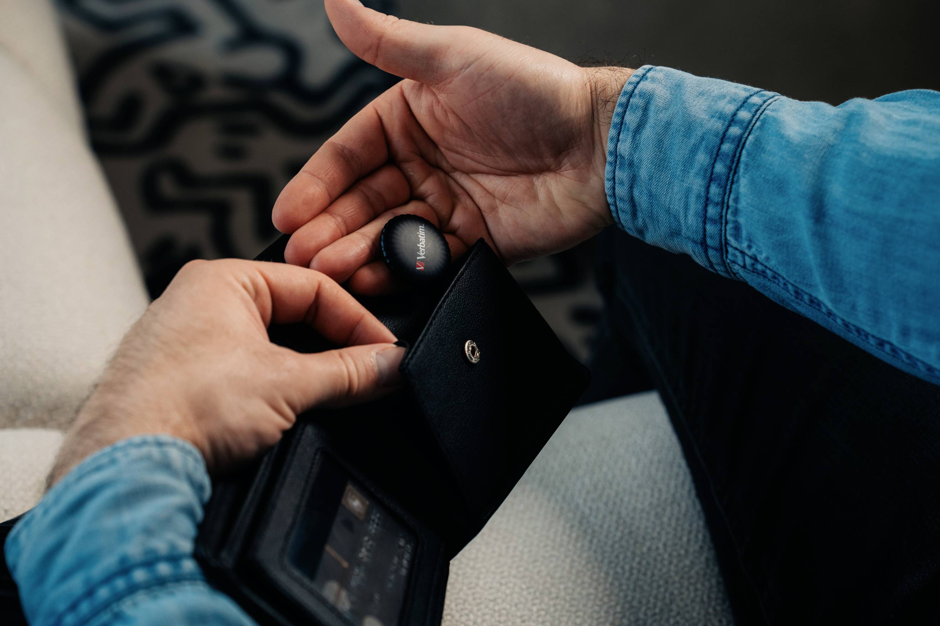 Une personne portant une chemise en jean tient un objectif noir et rond dans une main et ouvre un étui noir de l'autre main.