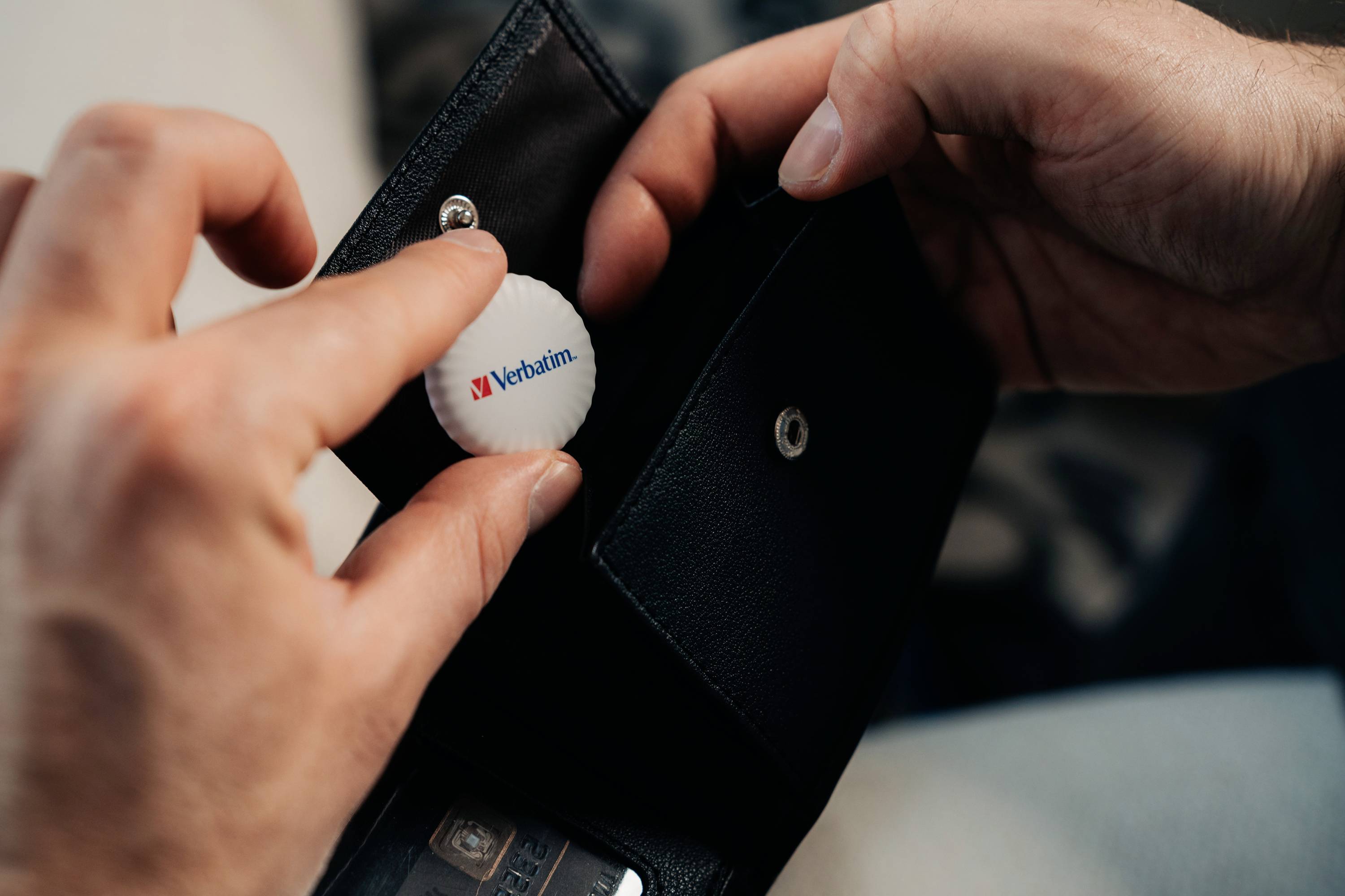 Une personne tient un portefeuille en cuir dans sa main tout en y glissant un objet blanc portant le logo 'Verbatim'.