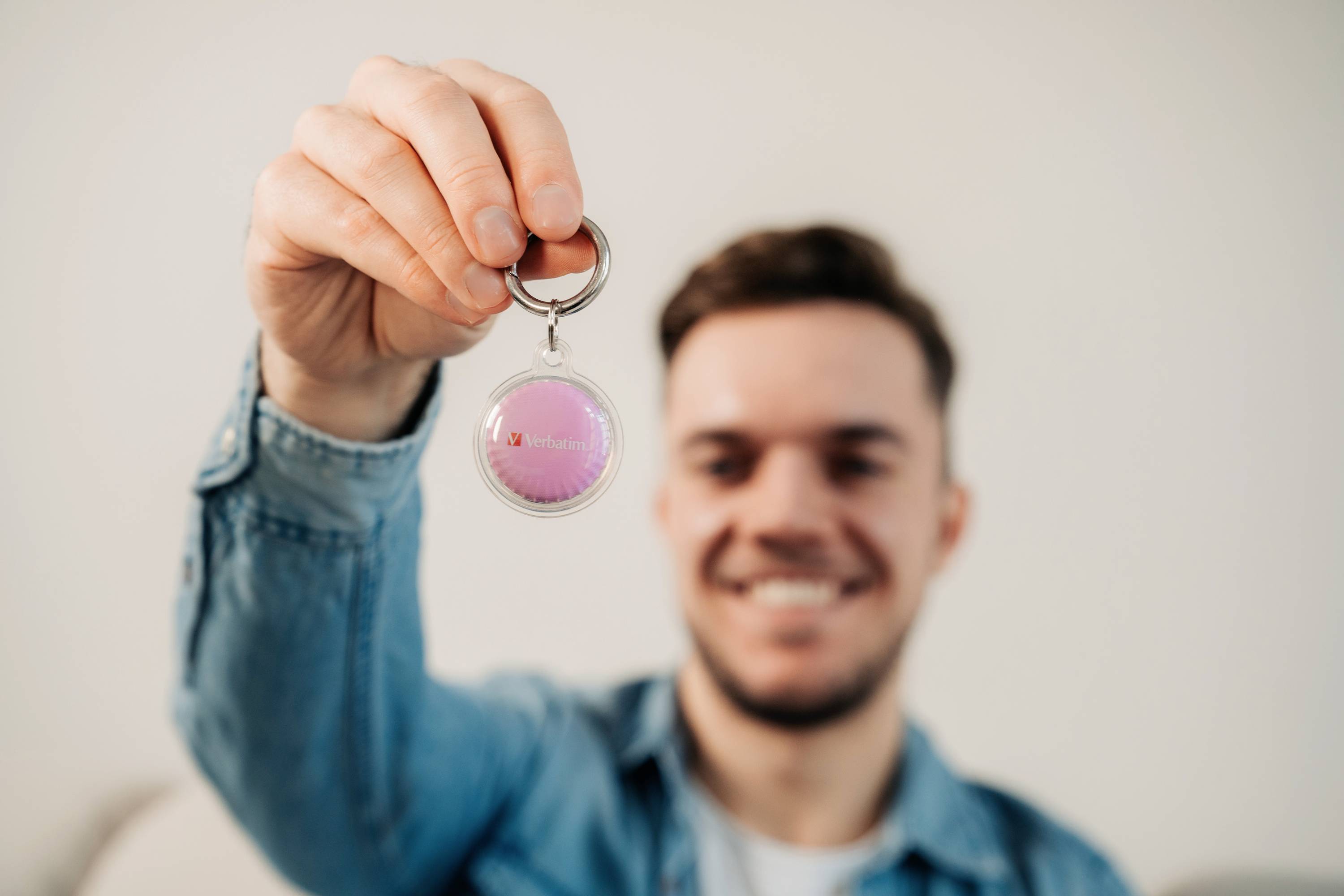 Un homme tient un porte-clés avec une surface rose et un petit symbole de cœur rouge devant l'objectif. L'arrière-plan est flou.