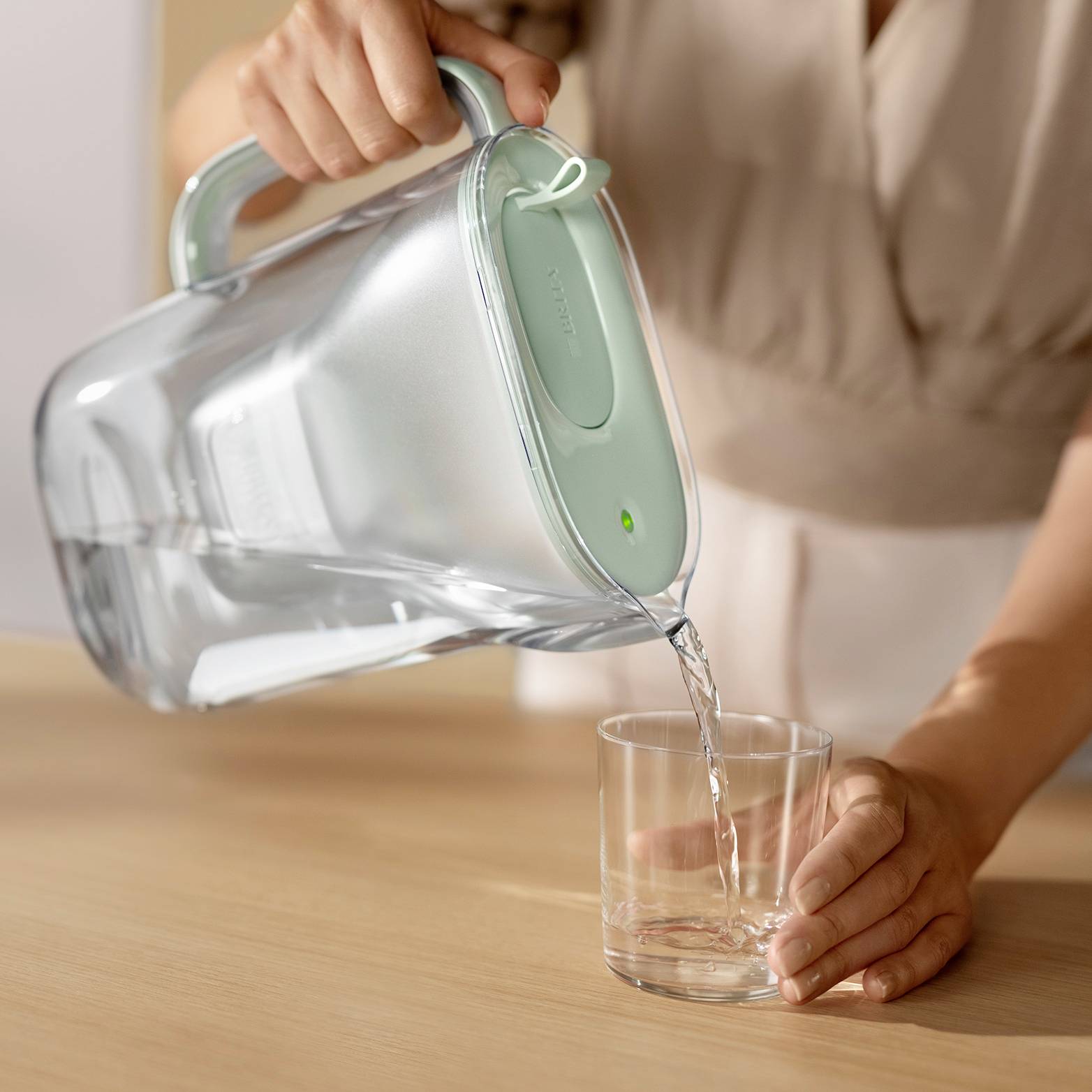 Une personne verse de l'eau d'une cruche dans un verre posé sur une table. L'image met l'accent sur l'action de verser.