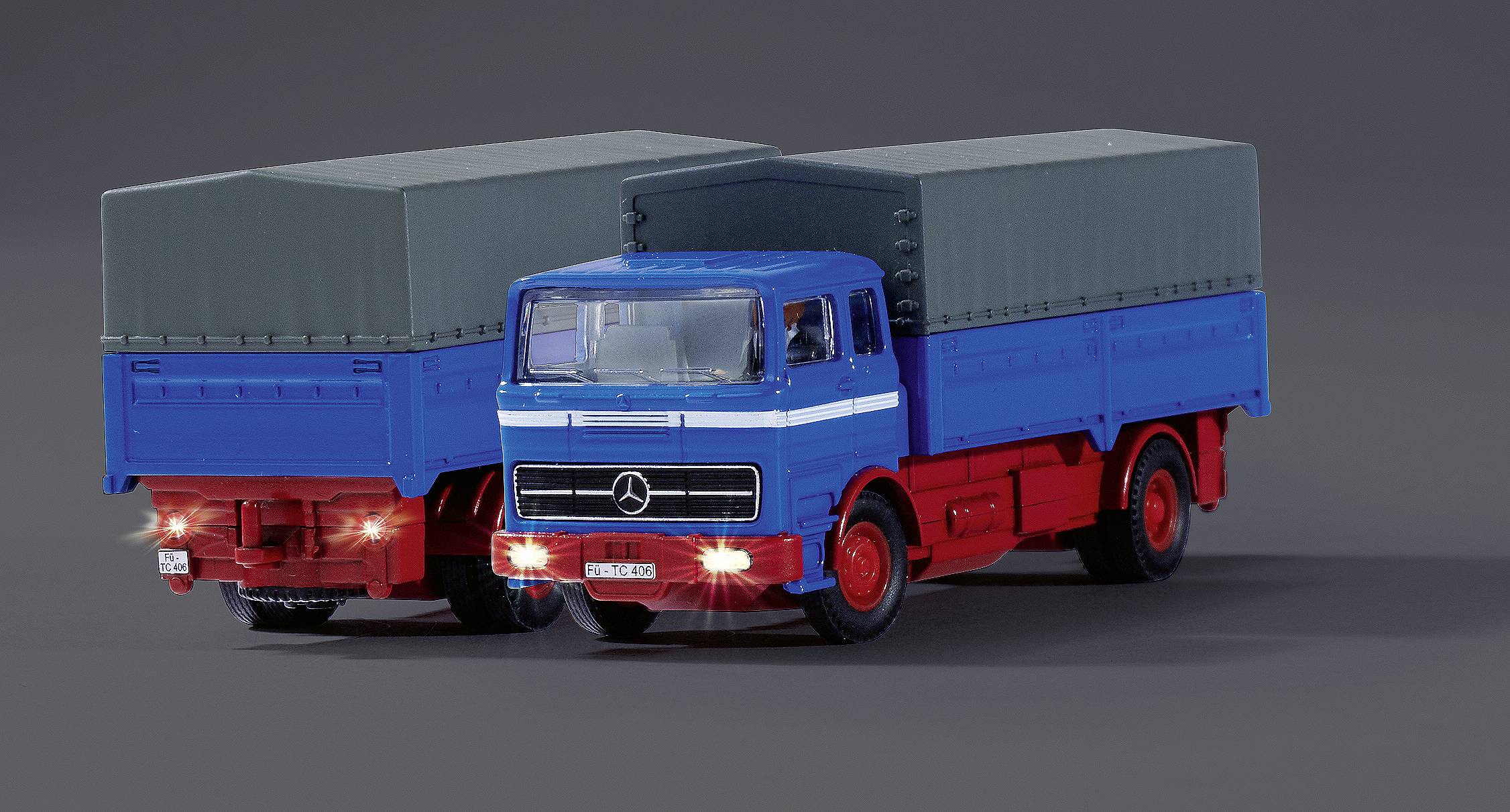 Deux camions-modèles avec des cabines de conducteur bleues et des superstructures rouges sur un fond gris. Les deux ont des bâches grises.