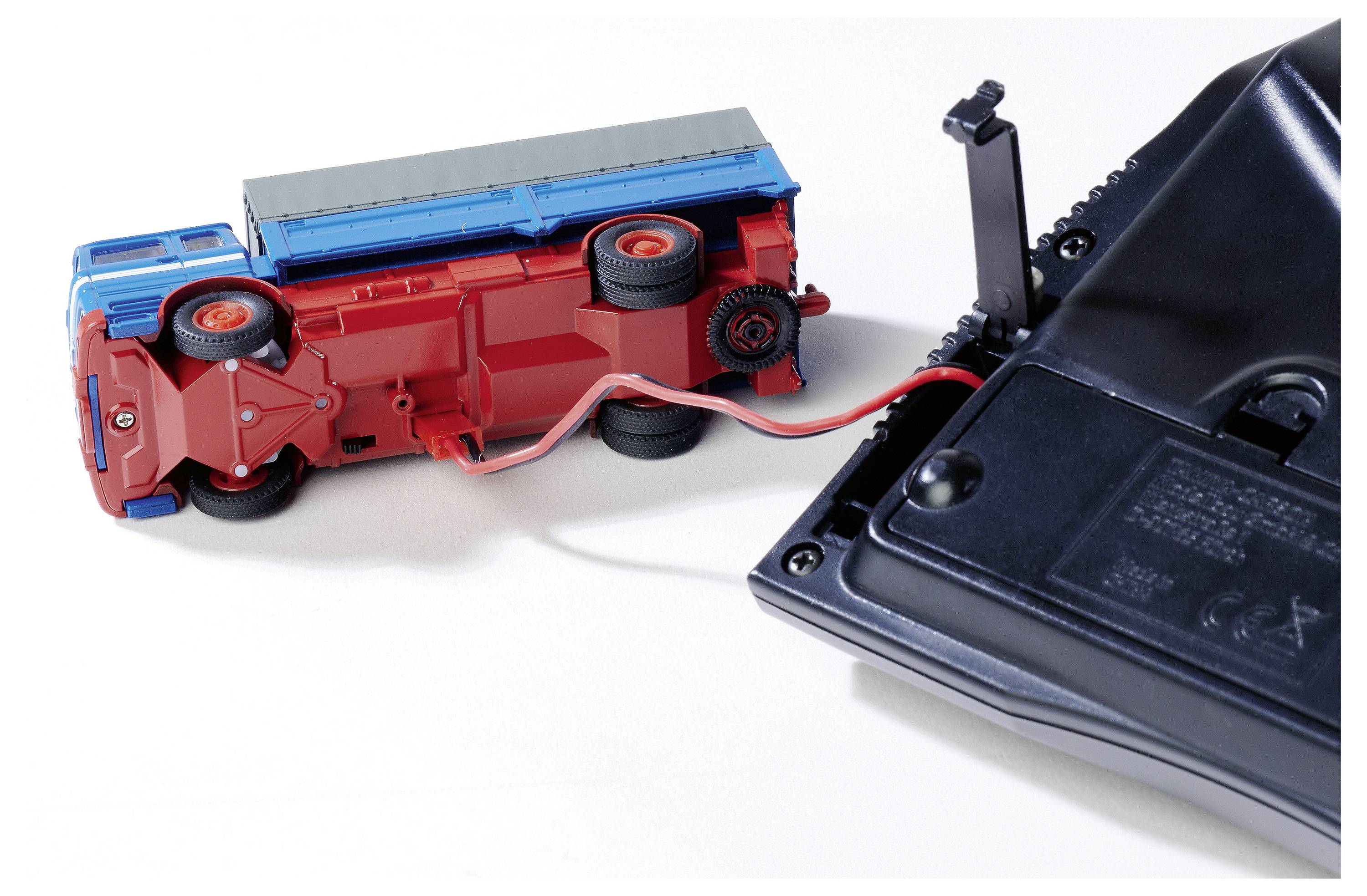 Un camion de pompiers en jouet renversé est connecté à un dispositif noir. Un câble rouge relie les deux objets.