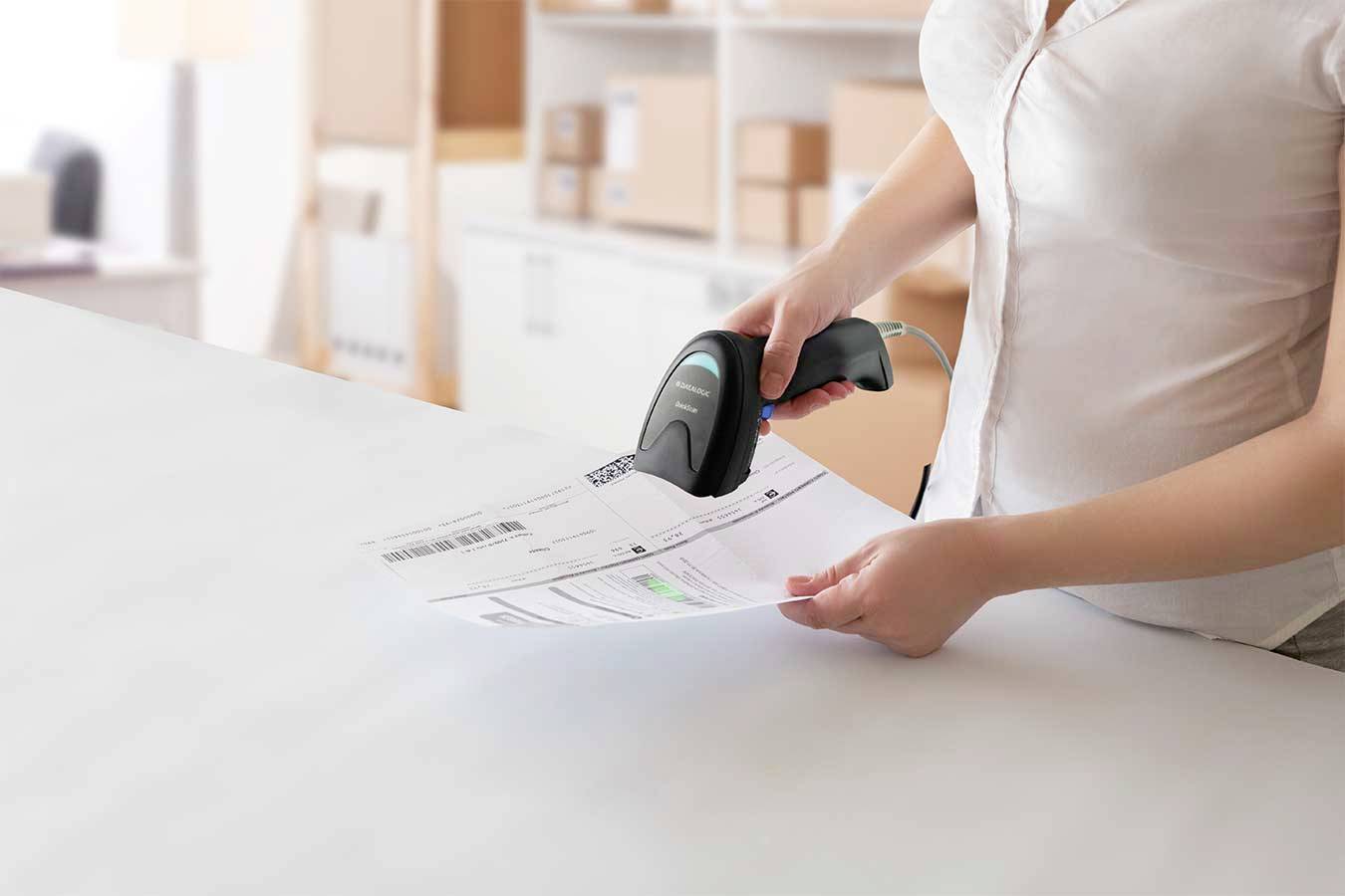 Une personne scanne un code-barres sur un document dans un bureau avec des cartons en arrière-plan.