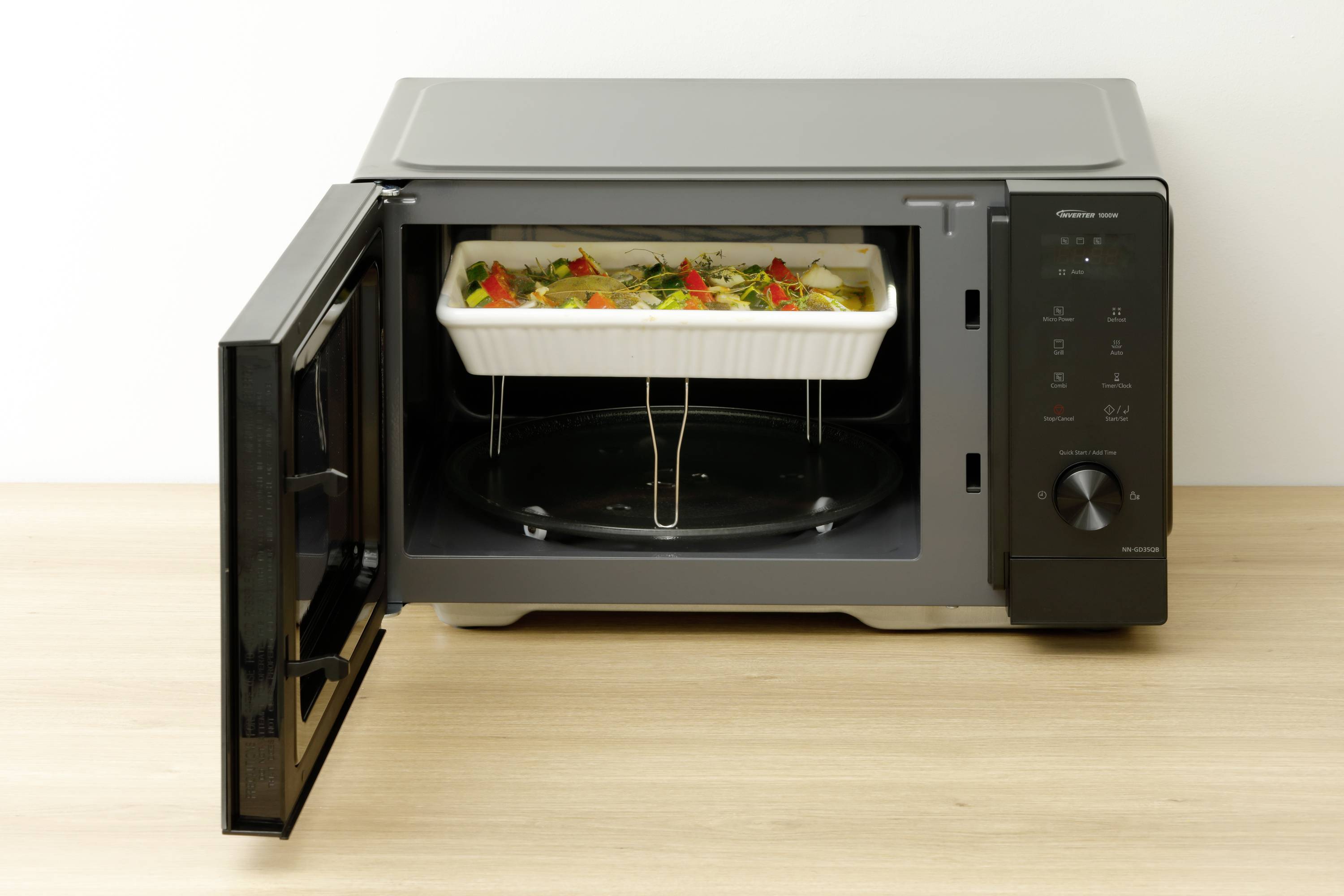 Un four à micro-ondes dont la porte est ouverte présente un plat gratiné au fromage et aux légumes dans un plat blanc sur un plateau tournant.