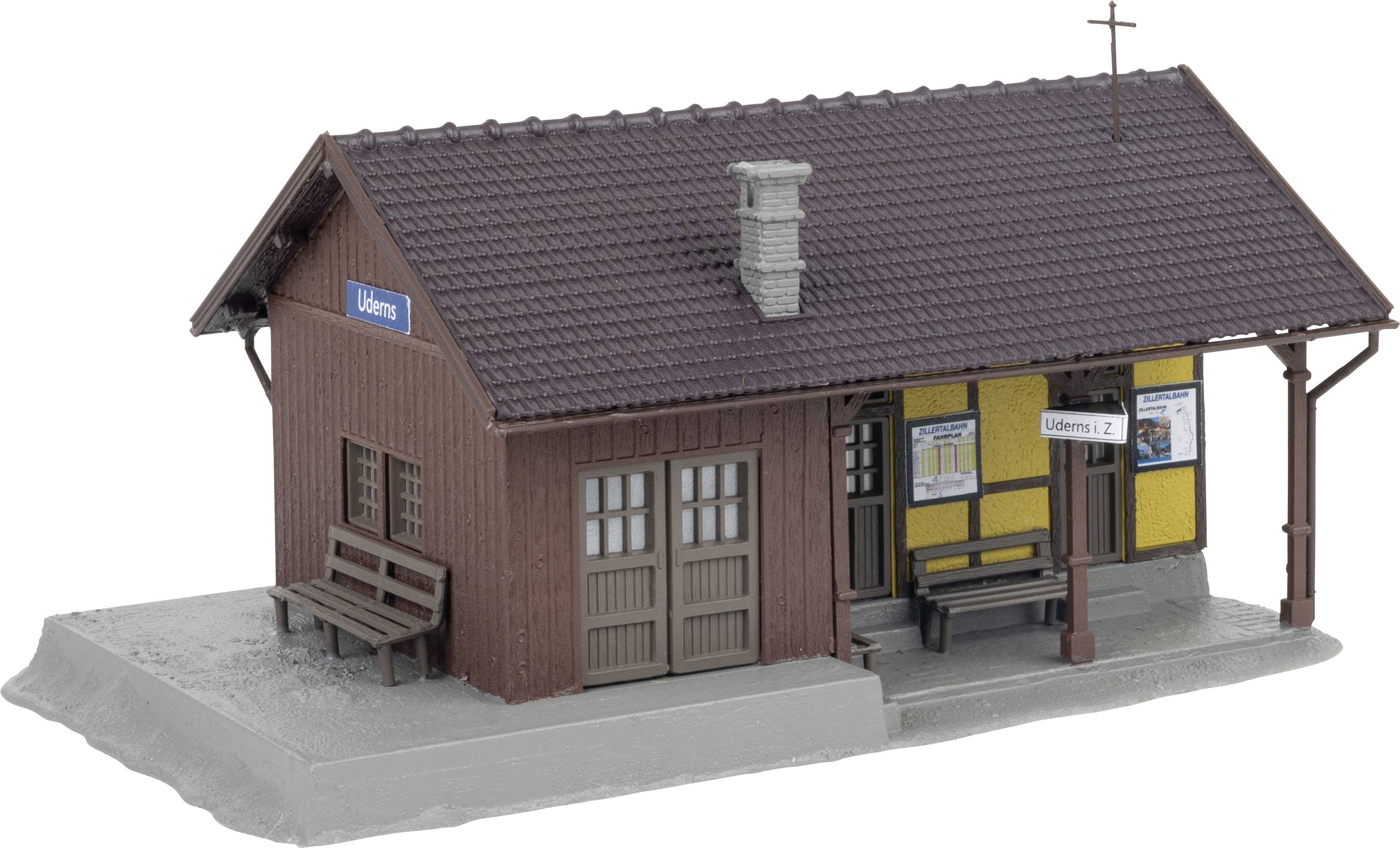 Un petit modèle d'un bâtiment de gare avec un revêtement en bois brun et un panneau 'Üdern'. Des panneaux et des bancs sont visibles.