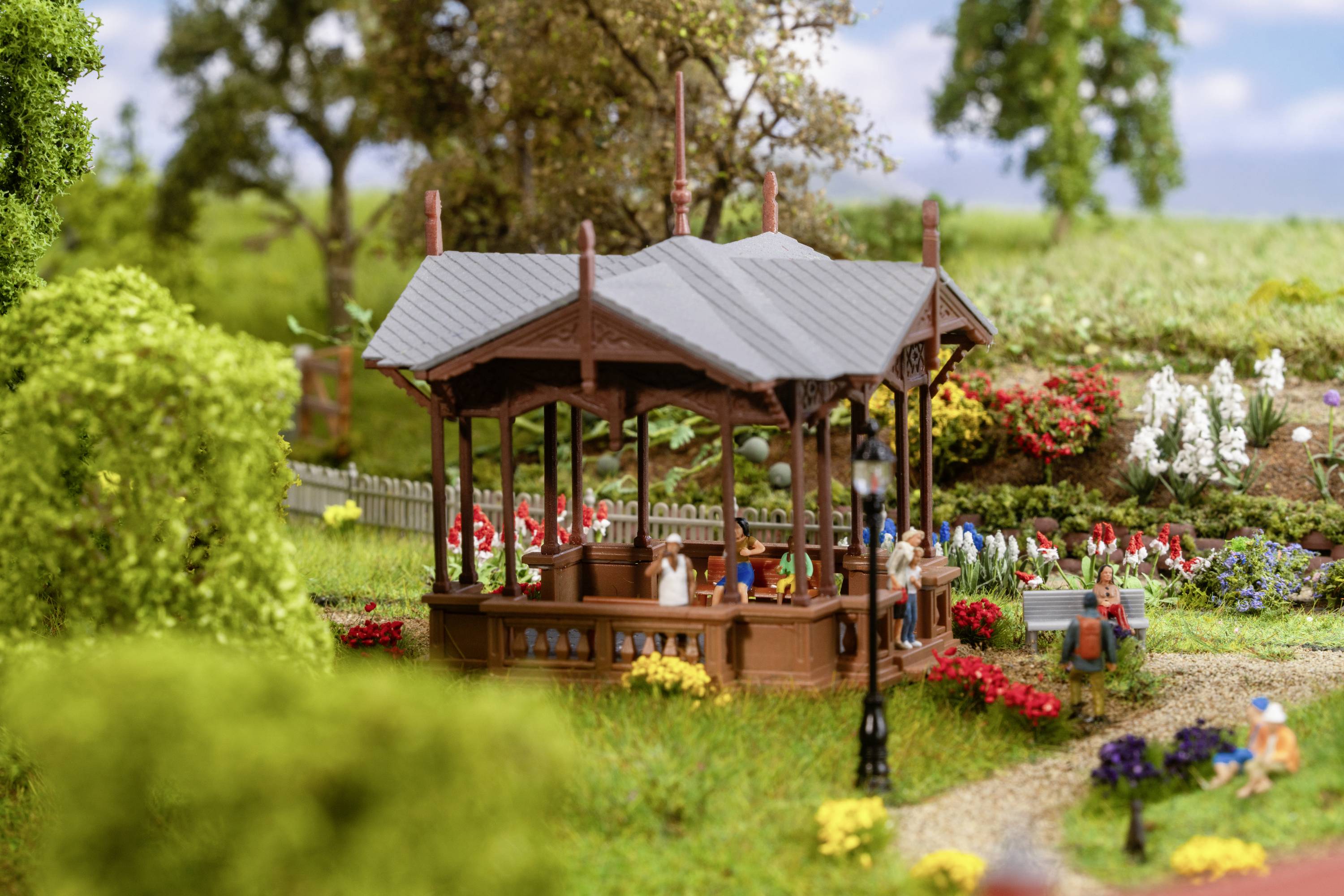 Un modèle d'un parc avec un pavillon au centre, entouré d'arbres, de fleurs et de figurines miniatures assises paisiblement dans le parc.