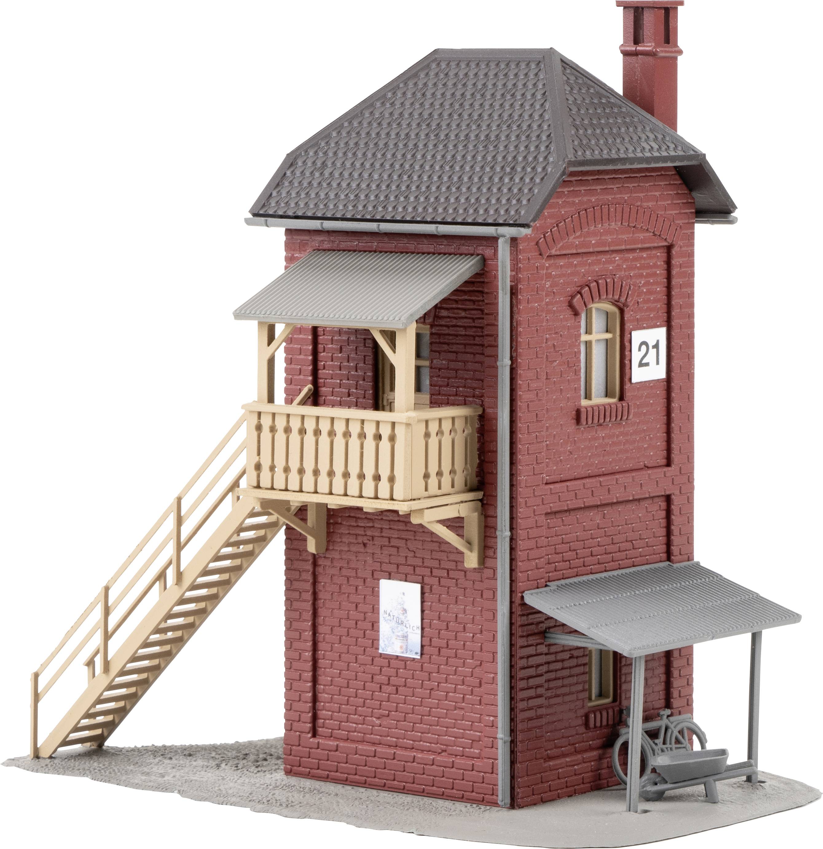 Un bâtiment en briques rouges au format miniature avec un balcon en bois et un escalier sur le côté, une petite remise et un vélo à proximité.