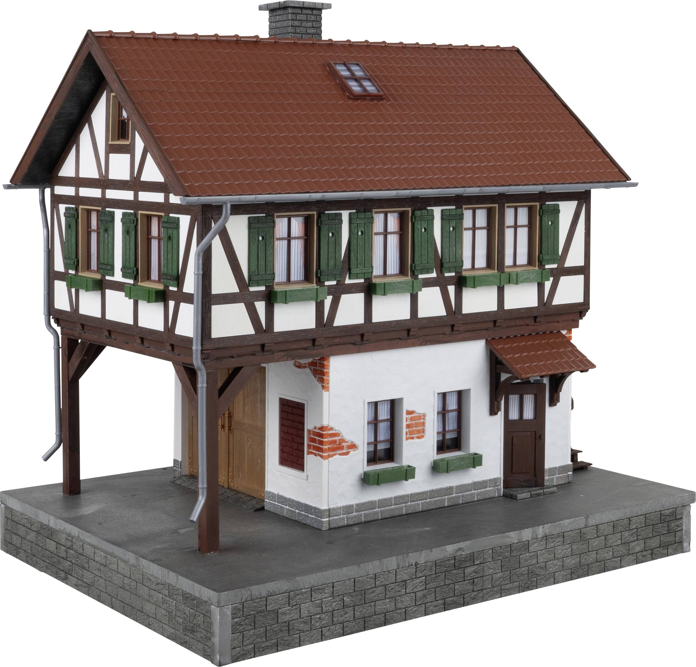 Une maison modèle de style à colombages avec un toit en tuiles rouges et des volets verts, posée sur un soubassement gris.