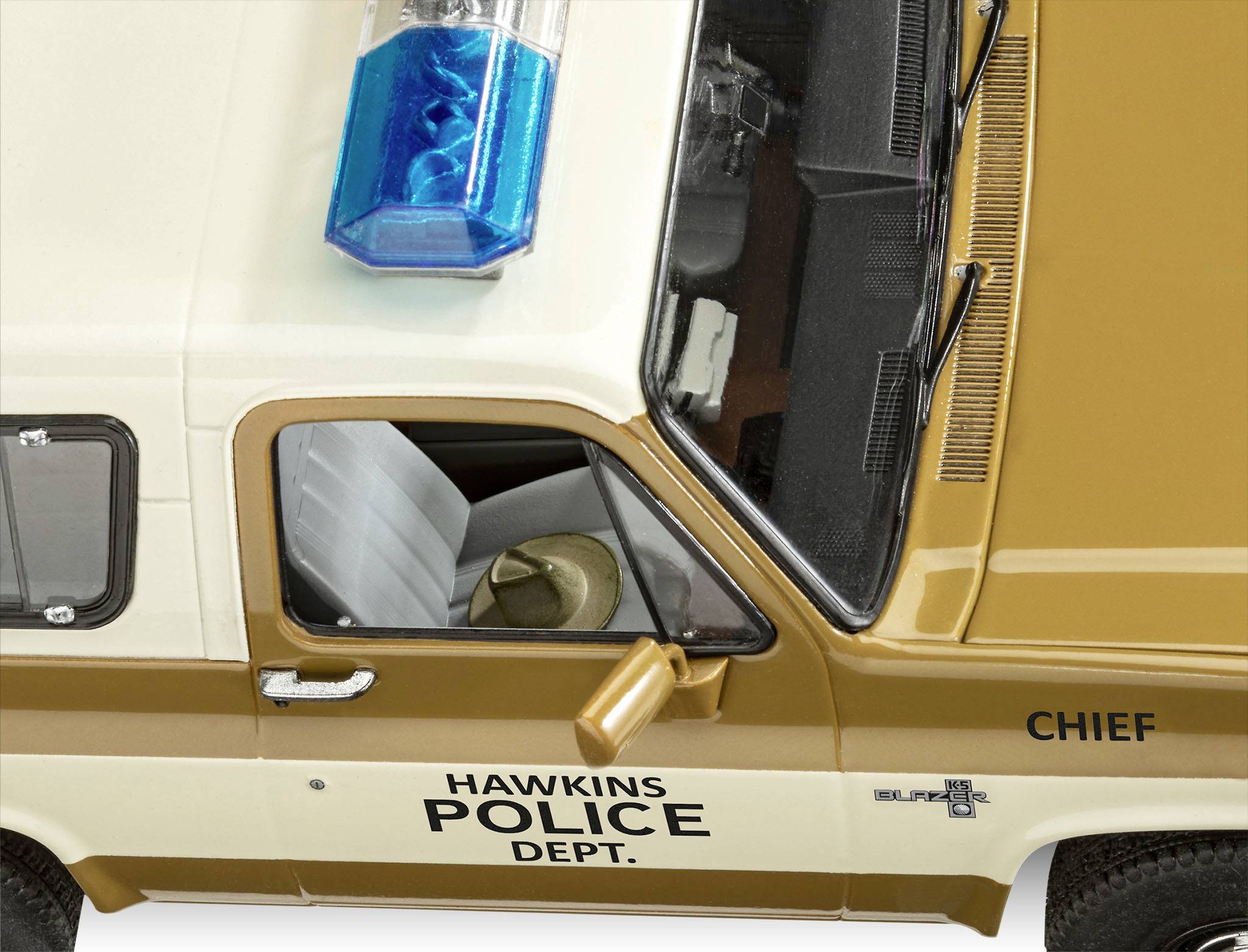 Un véhicule de police couleur crème portant l'inscription 'Hawkins Police Dept.' et 'Chef' sur la portière. Une rampe lumineuse bleue est visible.