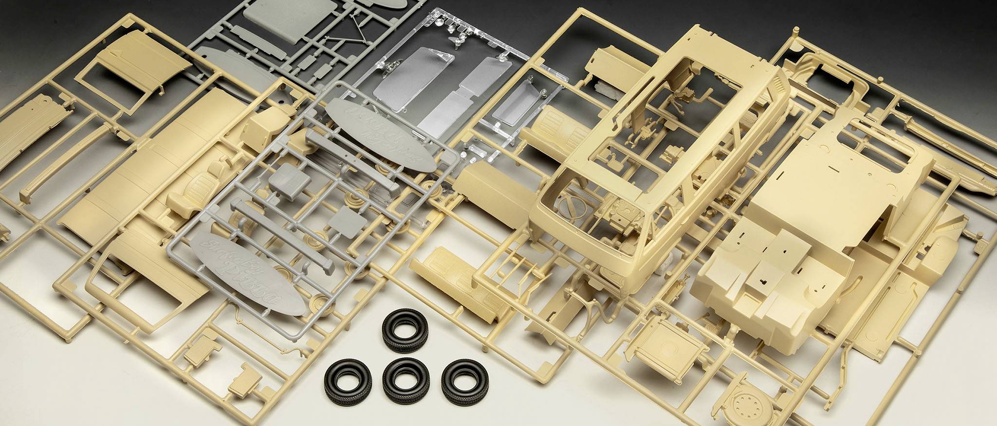 Plusieurs pièces de maquette en plastique non assemblées de couleur beige et grise, accompagnées de quatre roues noires, réparties sur une table.