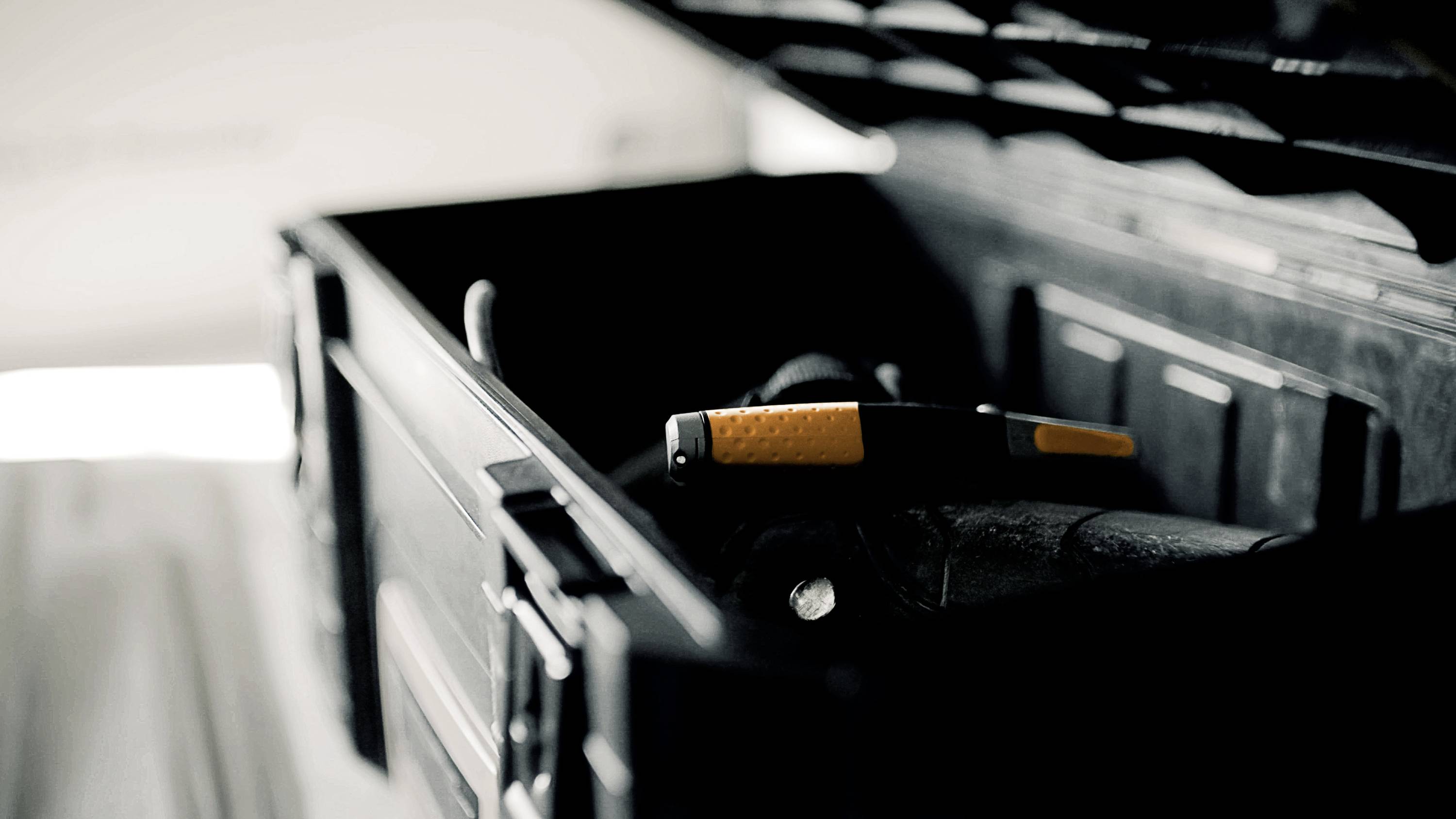 Une boîte à outils ouverte avec un marteau orange et noir au premier plan, dans une pièce faiblement éclairée.