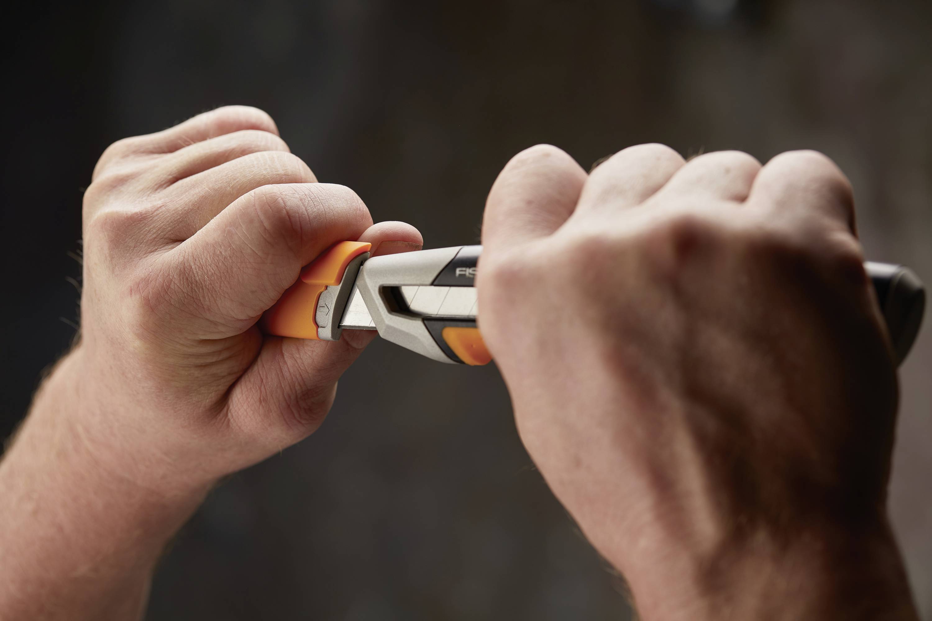 Deux mains utilisent une pince pour maintenir une pièce orange. L'arrière-plan est flou.