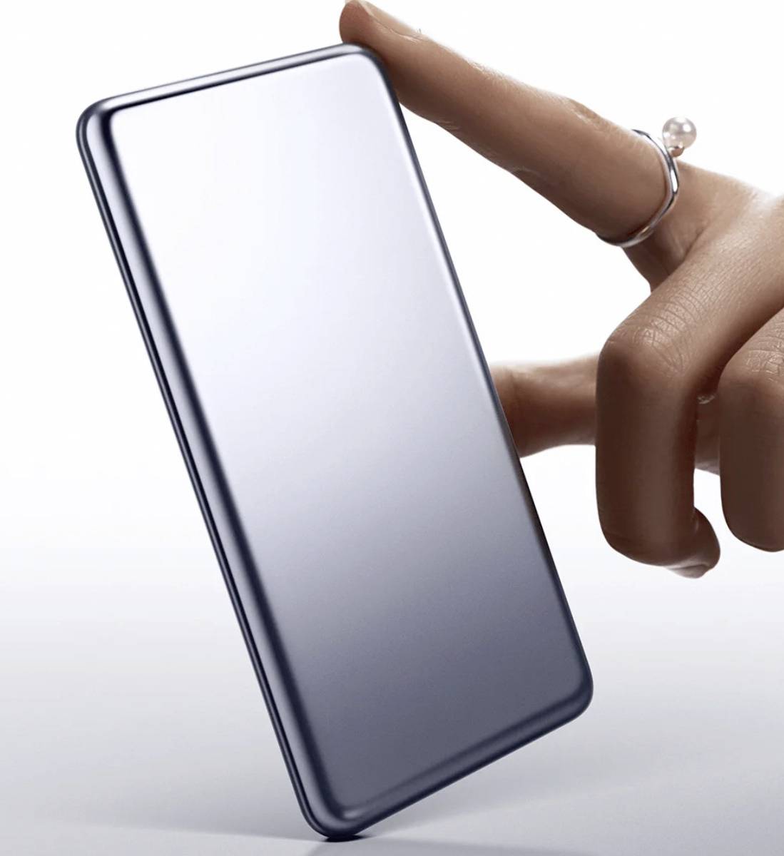 Une main portant une bague tient un smartphone moderne et élégant, mettant en valeur son profil fin et son design métallique.