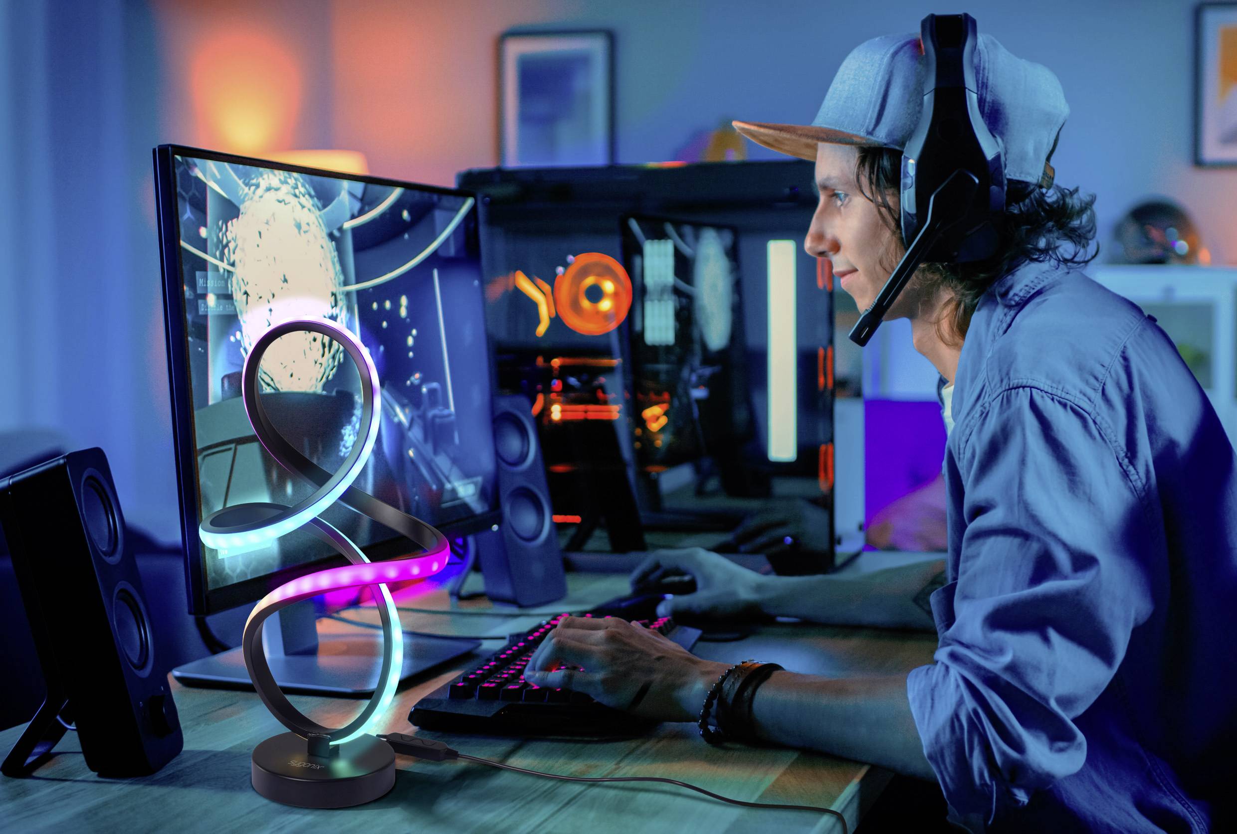 Une personne portant un casque joue à un jeu vidéo sur un ordinateur, entourée d'un setup de jeu coloré et lumineux dans une pièce faiblement éclairée.