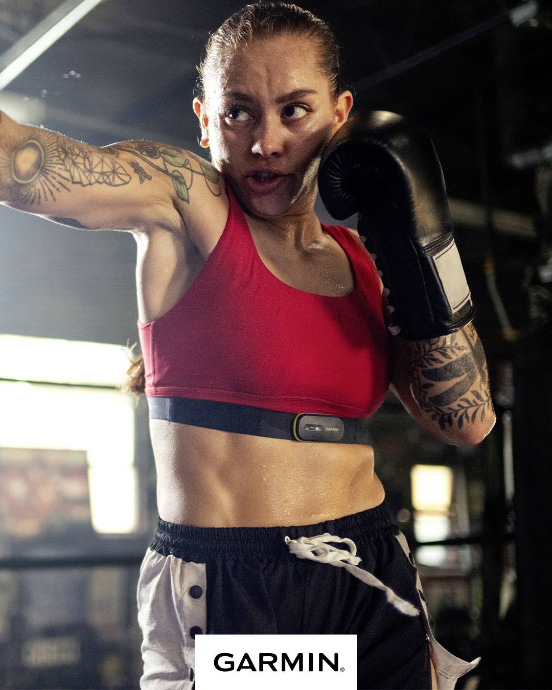 Une femme en tenue de sport boxe avec une expression concentrée. Elle porte un tracker de fitness. Au premier plan se trouve le logo 'GARMIN'.