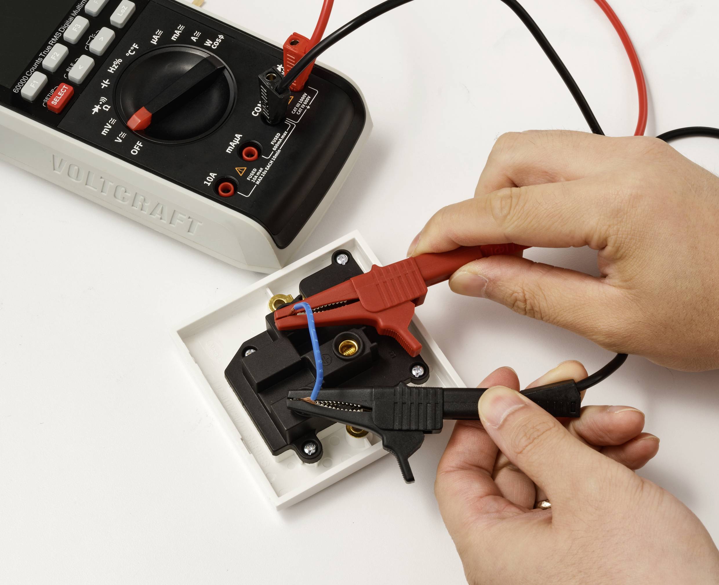Une personne utilise un multimètre pour tester une prise murale, en plaçant les sondes rouge et noire sur les fils, afin de vérifier la sécurité et le bon fonctionnement électrique.