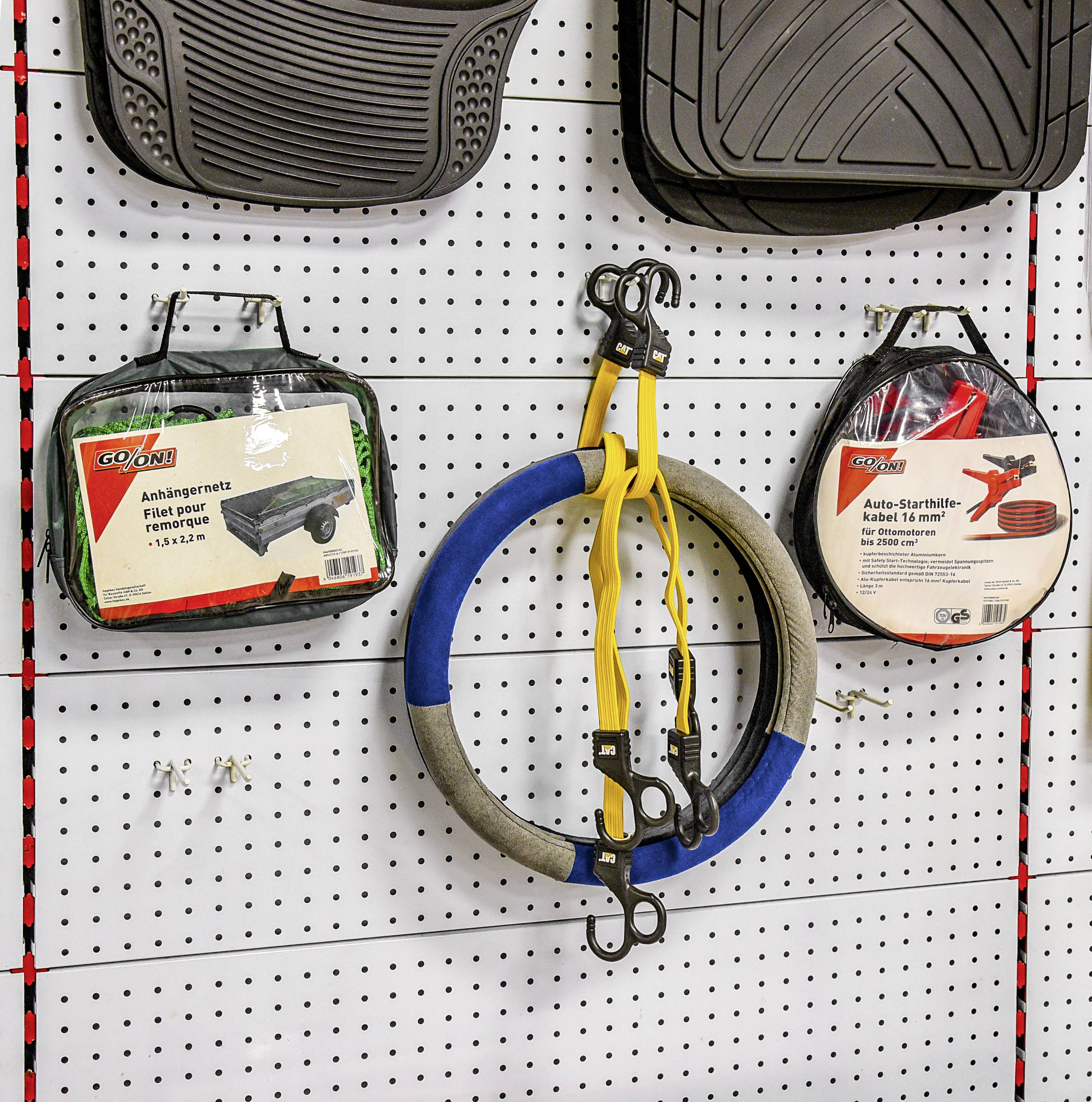 « Affichage mural avec divers accessoires automobiles : deux chaînes à neige emballées et une boucle de câble de remorquage jaune, suspendus sur un panneau perforé. »