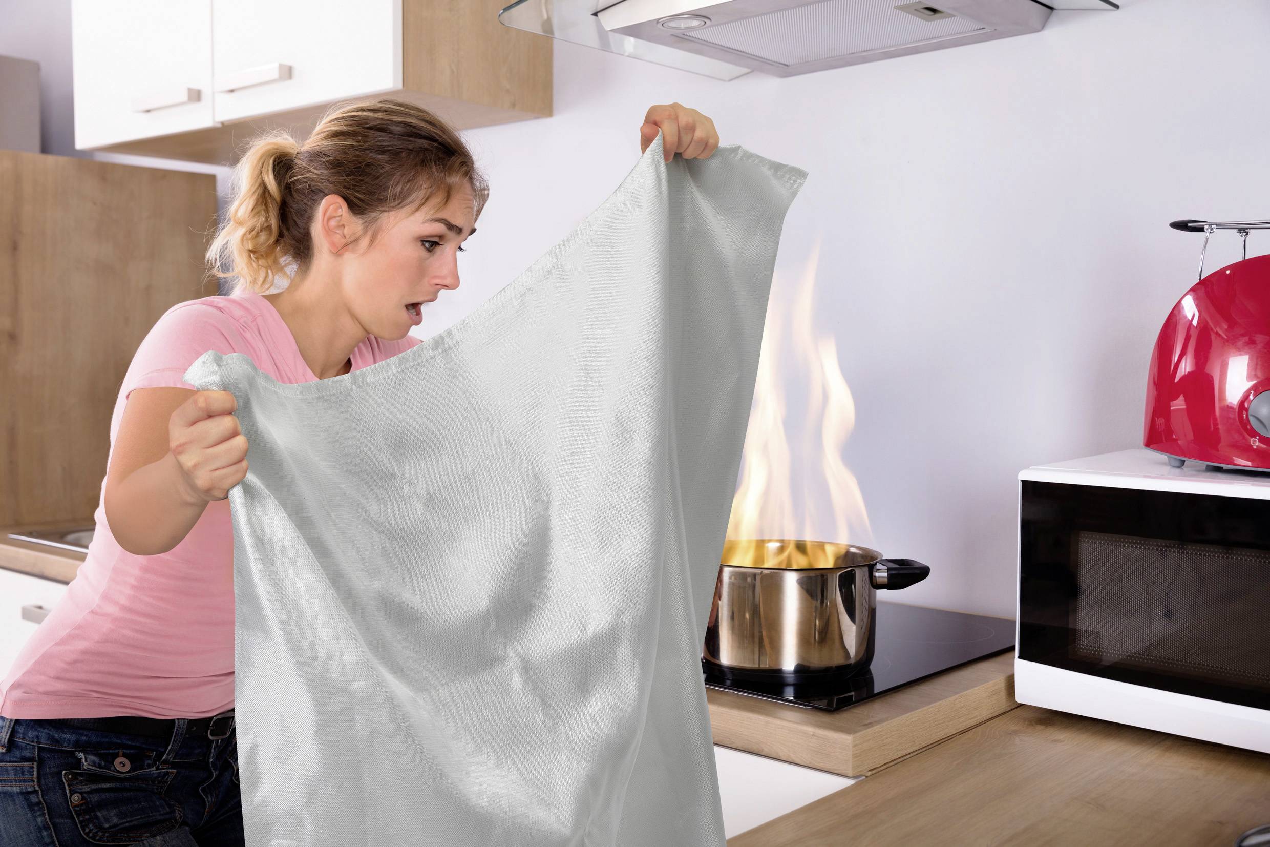 Une femme semble alarmée tout en tenant un chiffon près d'une casserole avec des flammes sur une cuisinière.