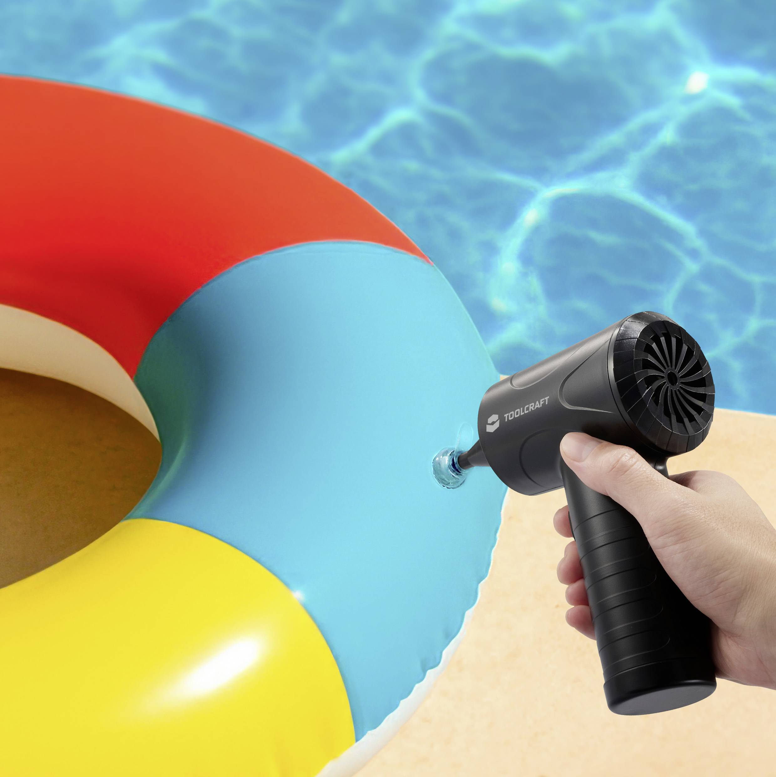 Une personne gonfle un matelas pneumatique coloré avec une pompe électrique à côté d'une piscine bleu vif.