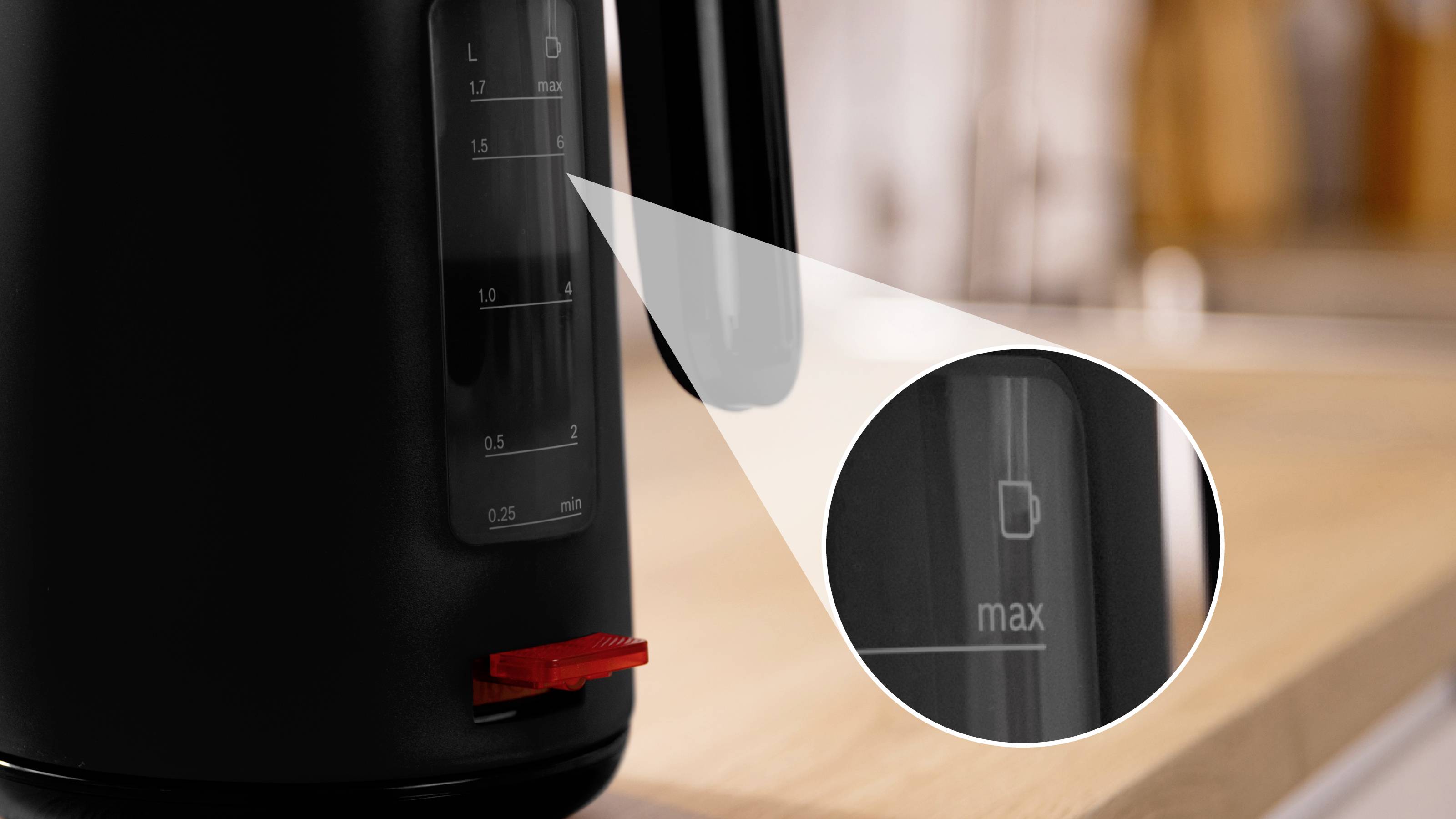 Une bouilloire électrique noire avec un gros plan sur l'indicateur de niveau d'eau montrant une ligne de remplissage maximale sur un comptoir en bois dans une cuisine.