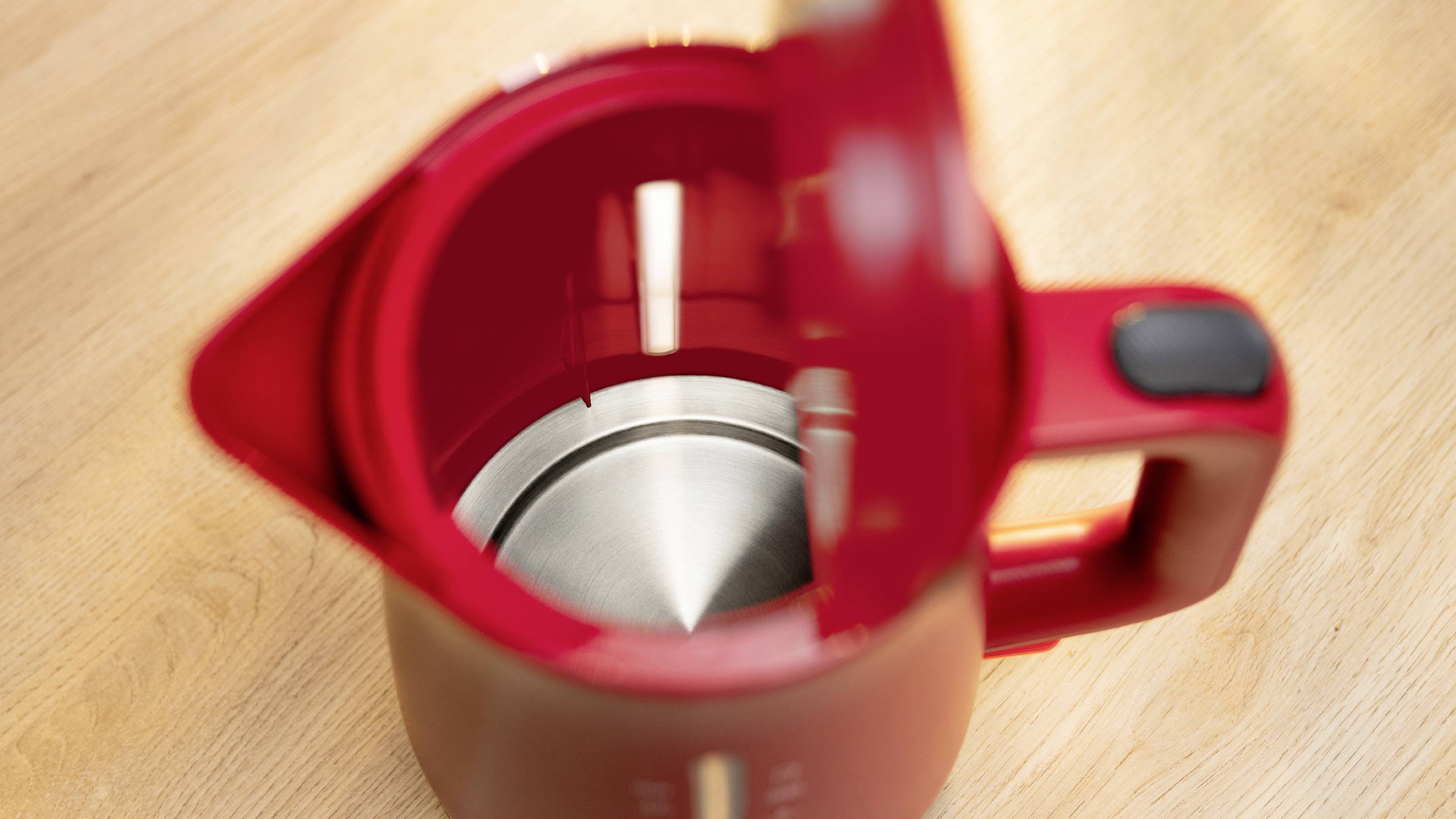 Une bouilloire électrique rouge dont le couvercle est ouvert, posée sur une surface en bois, laissant apparaître un intérieur en acier inoxydable.