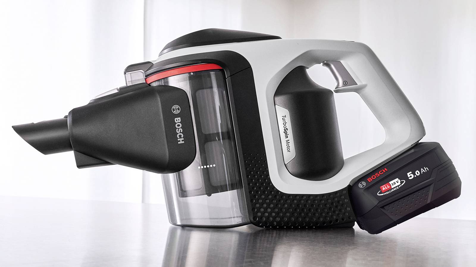 Aspirateur portable Bosch avec un réservoir à poussière transparent, buse noire et batterie amovible. Adapté aux petites tâches de nettoyage.