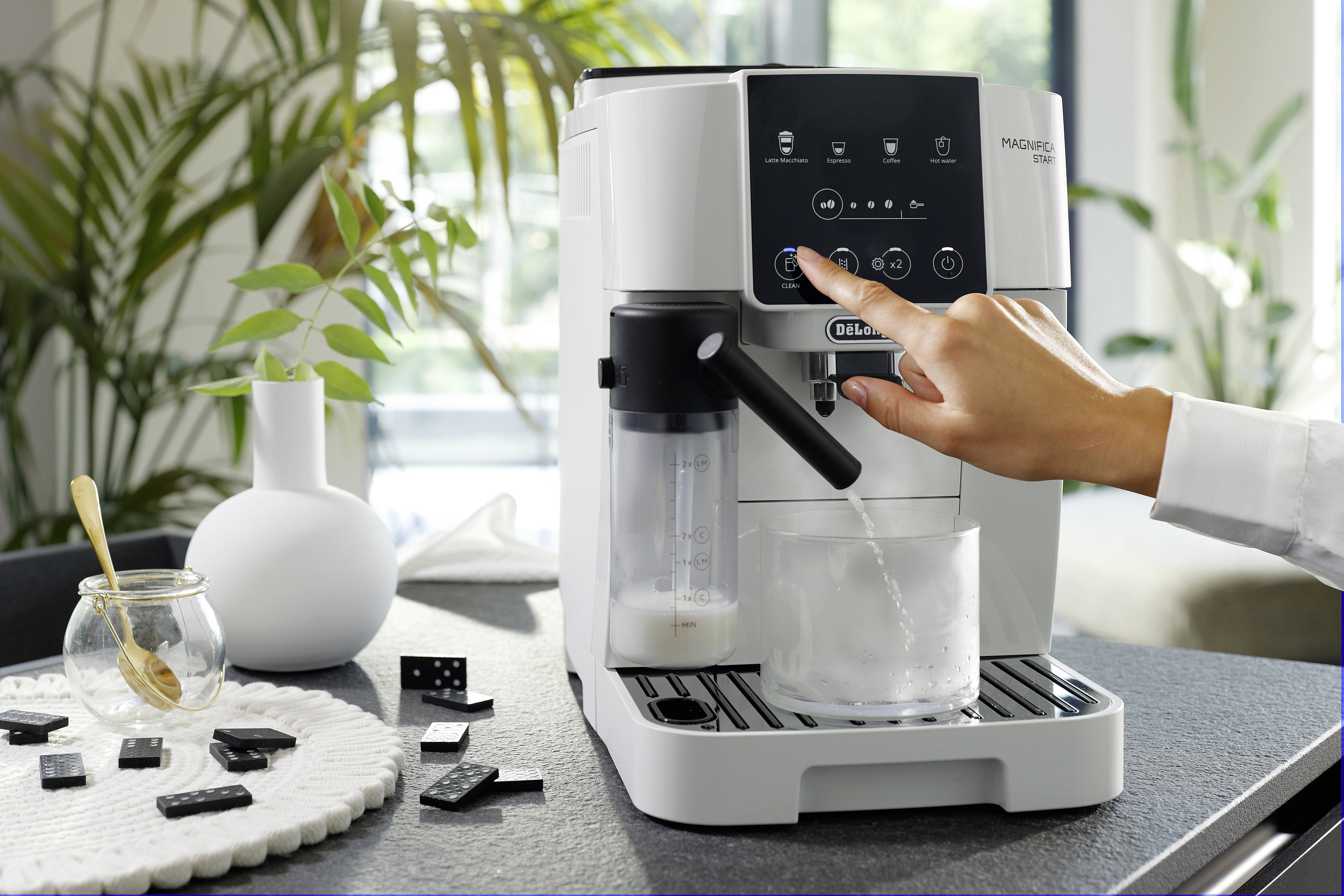 Une main actionne une machine à espresso moderne pour préparer du café. Un mousseur à lait et un plateau de dominos sont visibles sur le comptoir.