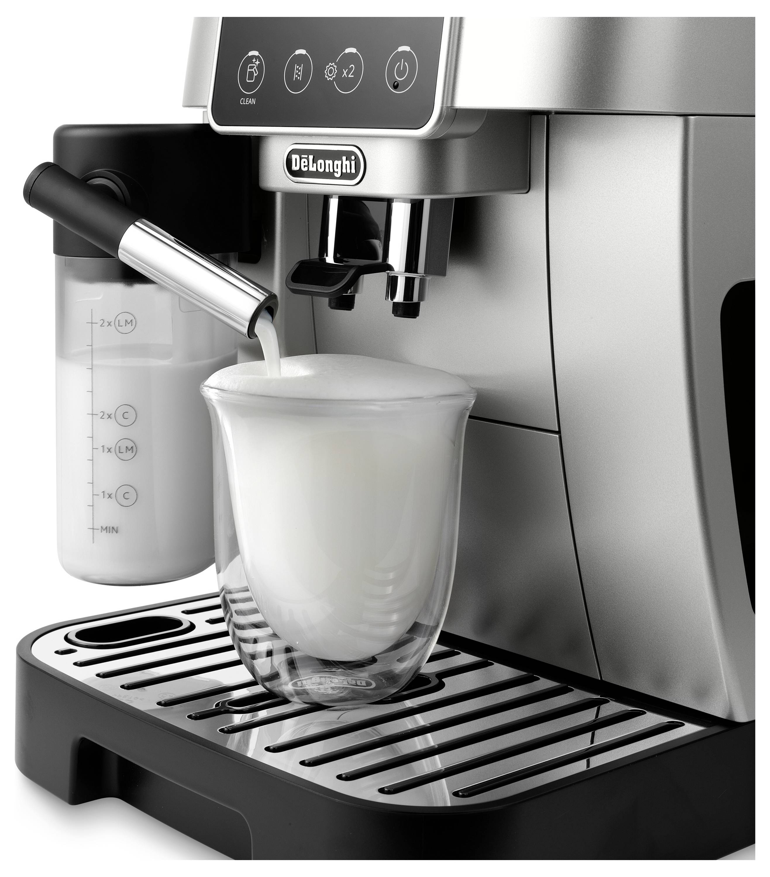Une machine à espresso en argent distribuant de la mousse de lait dans une tasse en verre transparente sur son plateau, avec un récipient à lait attaché sur le côté.