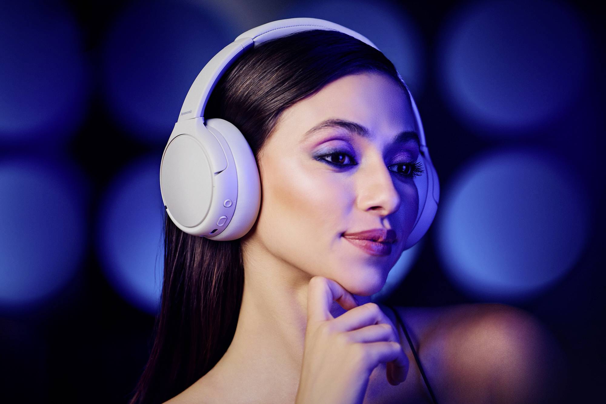 Une personne portant des écouteurs circumauriculaires profite de la musique, avec une expression sereine, sur un fond bleu estompé, transmettant un sentiment de calme.