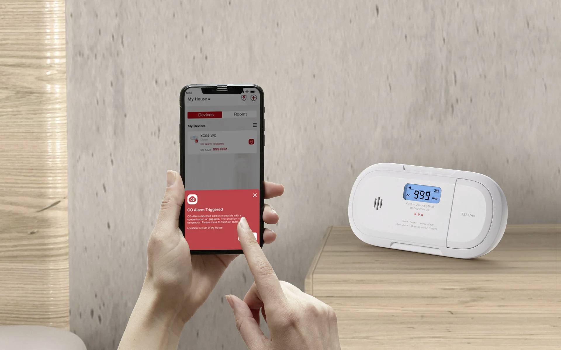 Un message « Alarme CO déclenchée » s'affiche sur un téléphone tenu par une personne, à côté d'un détecteur numérique de monoxyde de carbone indiquant « 999 ppm ».