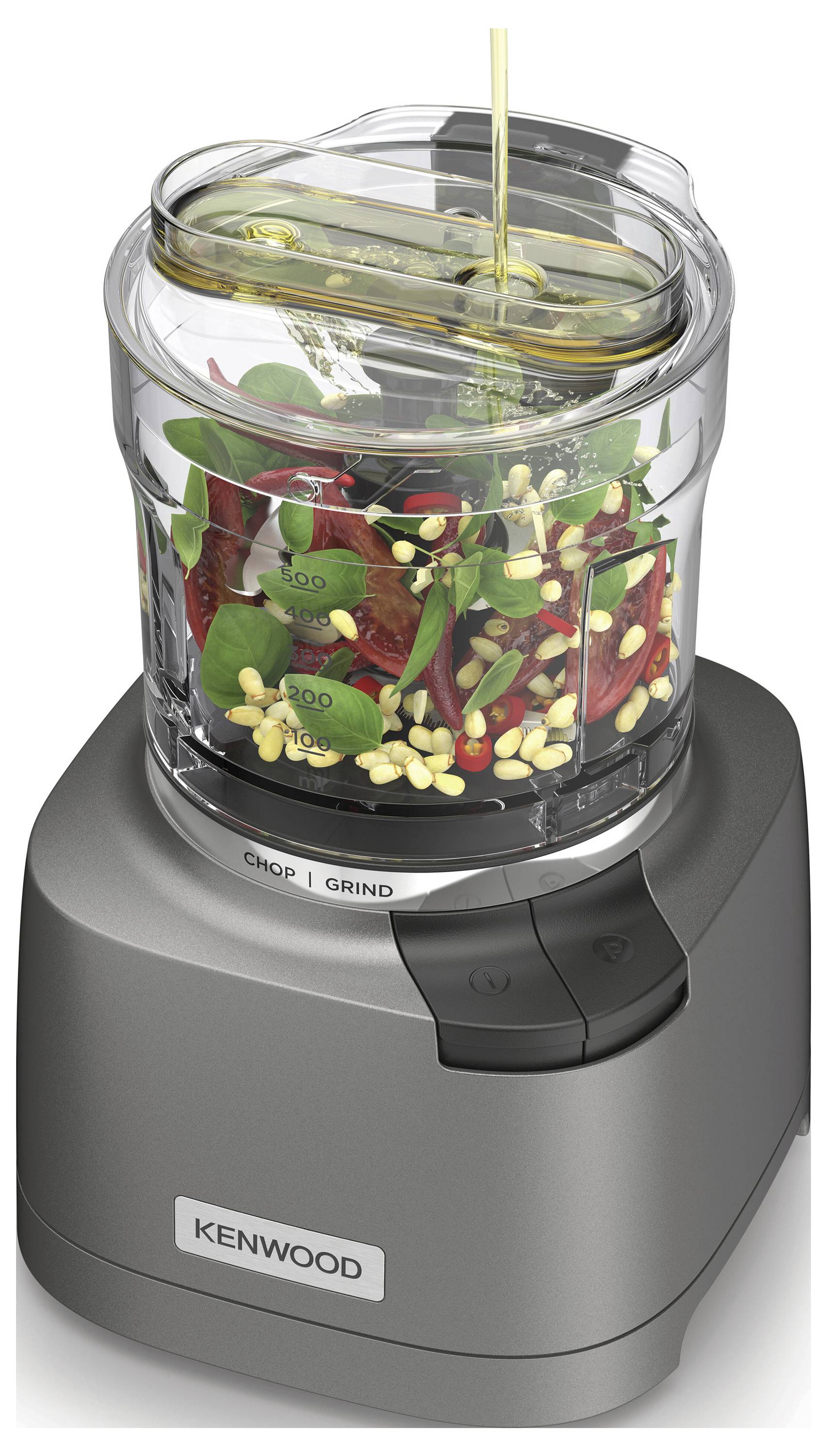 Un robot culinaire compact Kenwood mélangeant des noix, des légumes verts et des tomates séchées. L'huile est versée à travers la petite ouverture du couvercle.