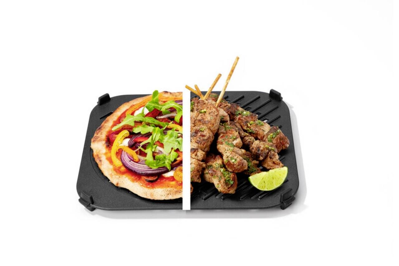 Une assiette divisée avec une pizza garnie de roquette et de poivrons sur la gauche, des kebabs grillés au citron vert sur la droite, posés sur une poêle carrée avec grille.