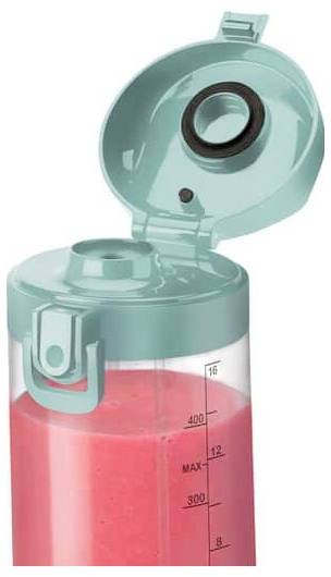 Un couvercle de blender turquoise ouvert sur un bocal de blender rempli de liquide rose ; des mesures en millilitres sont visibles sur le côté.